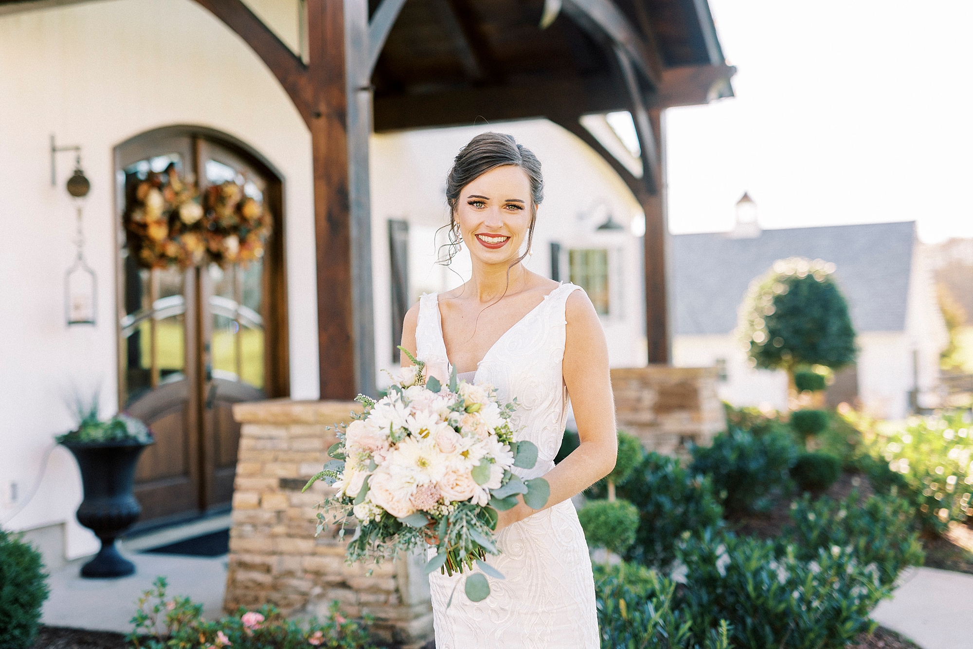 bride stands holding pink and white bouquet by wooden pillars at Chickadee Hill Farms