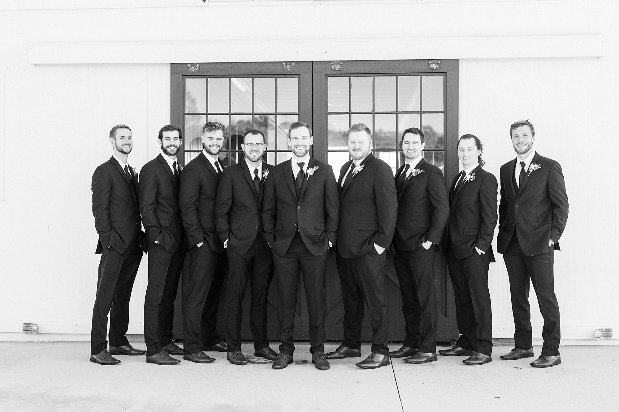 groom stands with groomsmen outside barn door at Chickadee Hill Farms