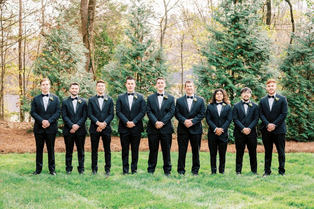 groom stands with groomsmen in black suits on lawn