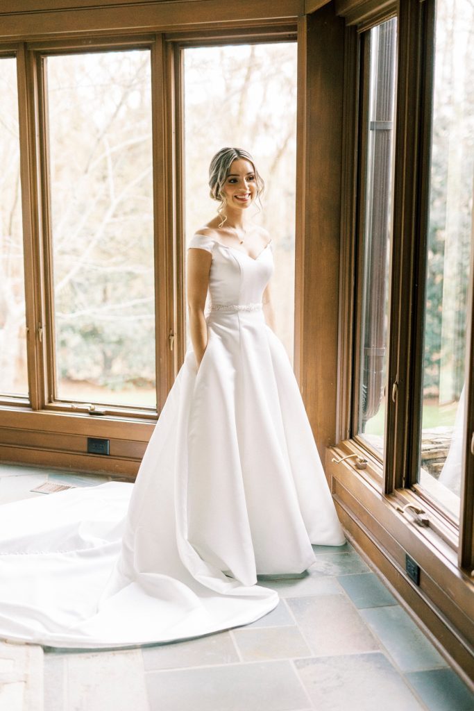 bride poses by long windows in wedding gown with pockets 