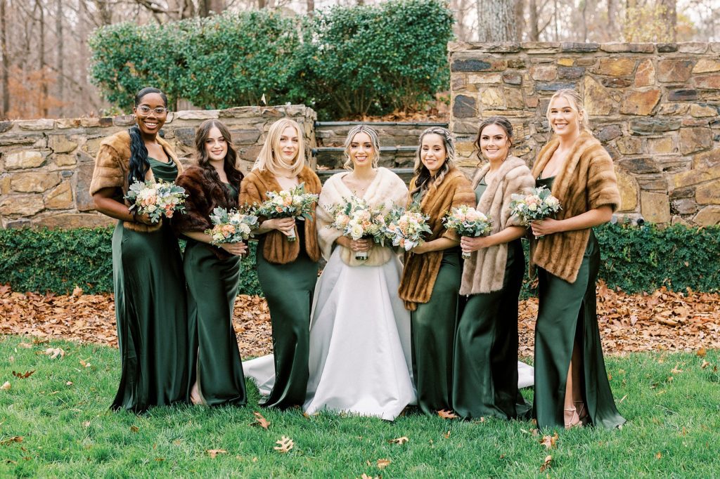 bride poses with bridesmaids in emerald green gowns with brown furs 