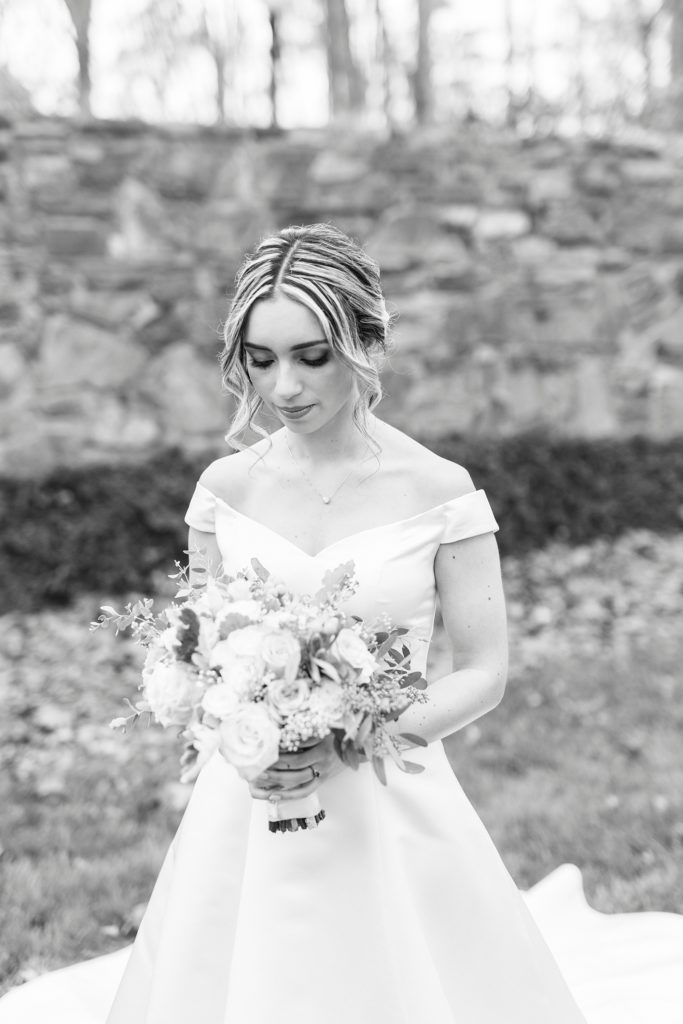 black and white portrait of bride looking down at bouquet with wedding gown skirt around her 