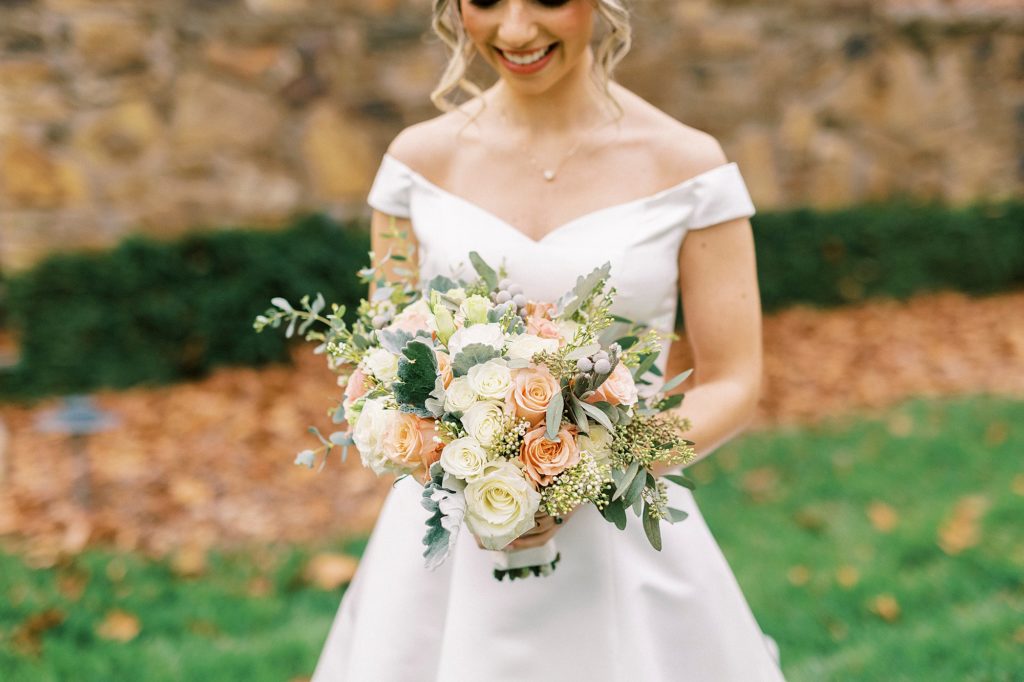bride holds bouquet of peach and ivory flowers in off-the-shoulder gown 