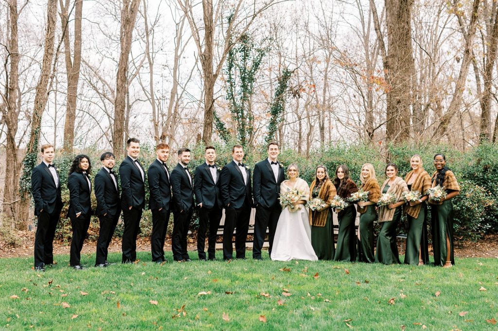 bride and groom stand with wedding party in black and emerald green attire 