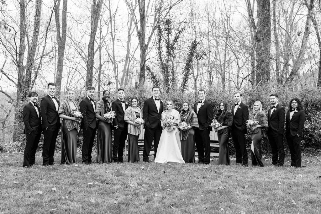 newlyweds stand with wedding party on lawn during fall wedding photos 