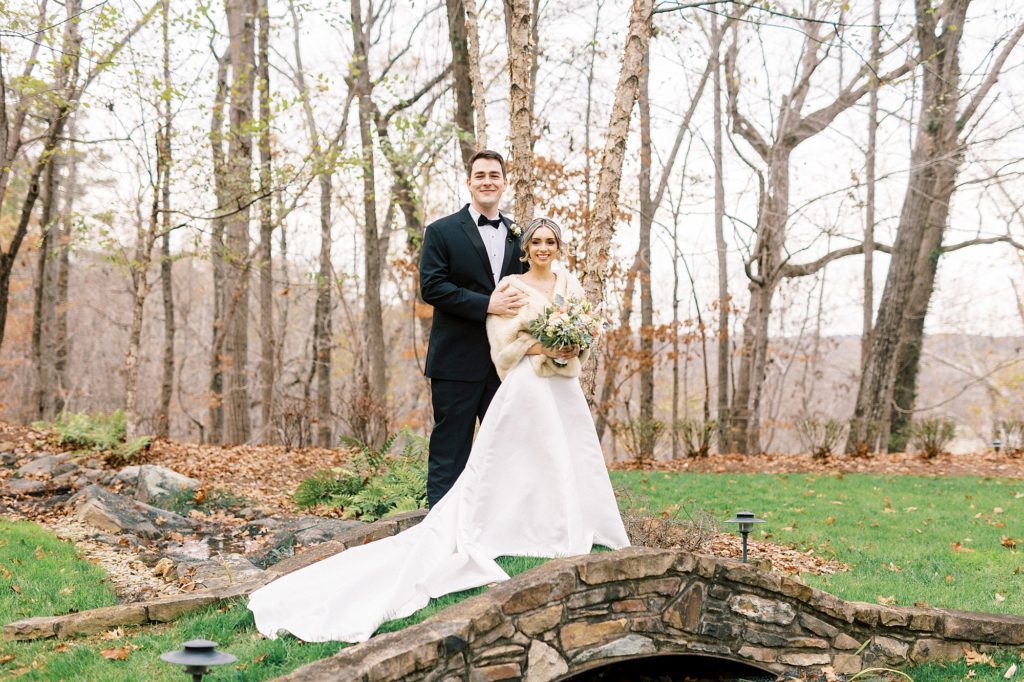 bride and groom hug on stone bridge during fall wedding photos 