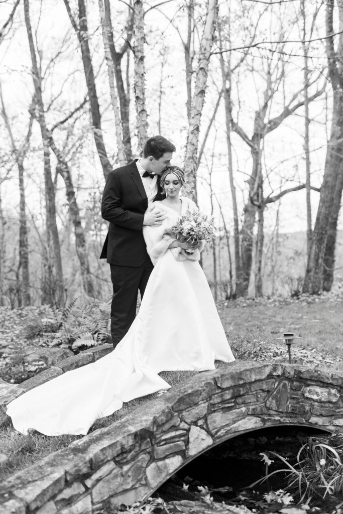 groom kisses bride's forehead standing on stone bridge 
