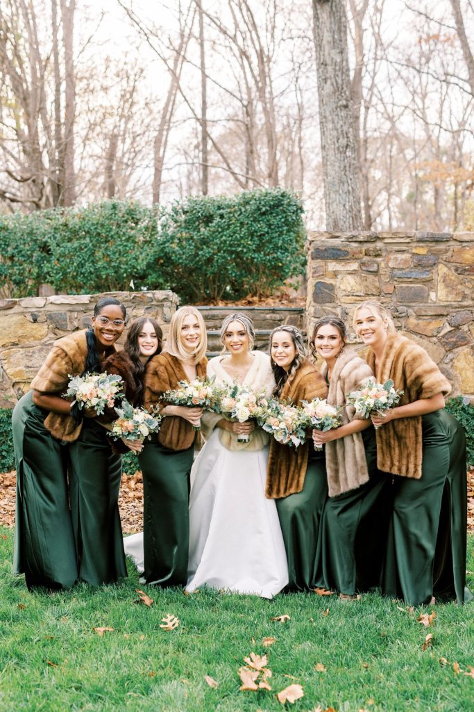 bride poses with bridesmaids in green gowns with brown furs 