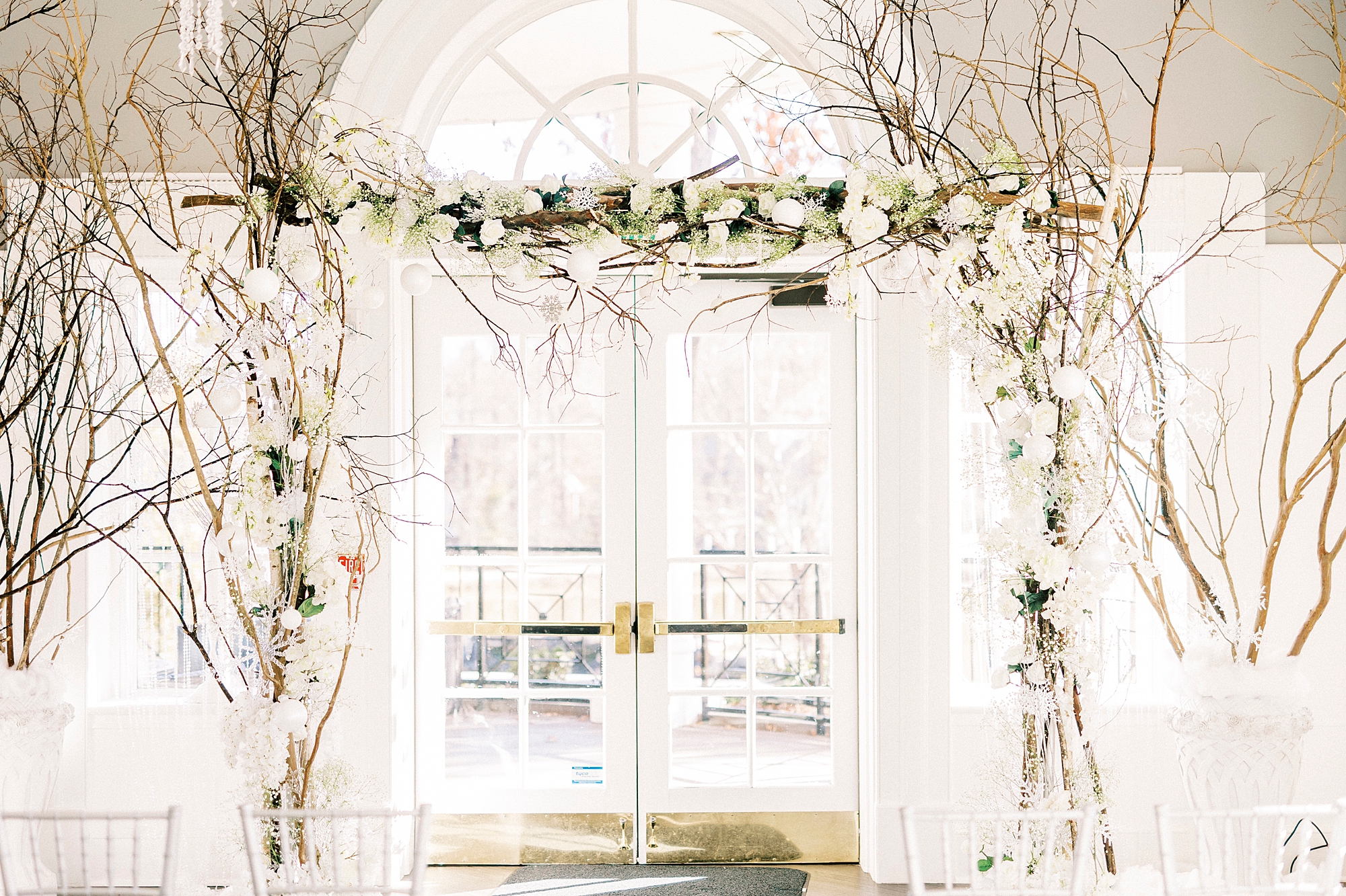 ceremony inside River Run Country Club with white florals and branches 