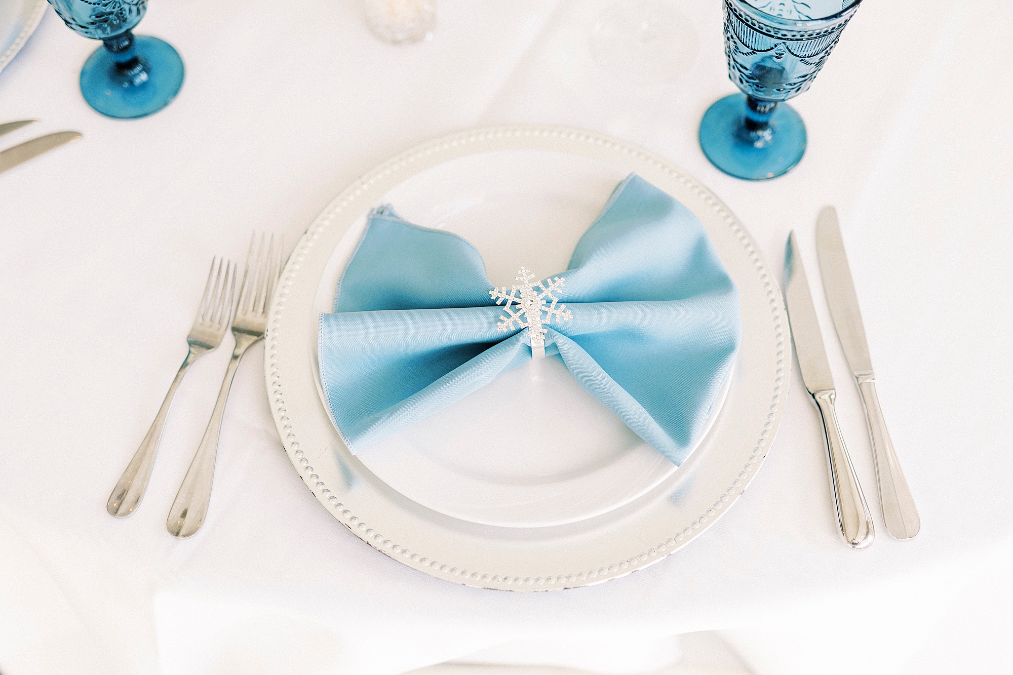 white and silver place setting with vintage blue glass and blue napkins
