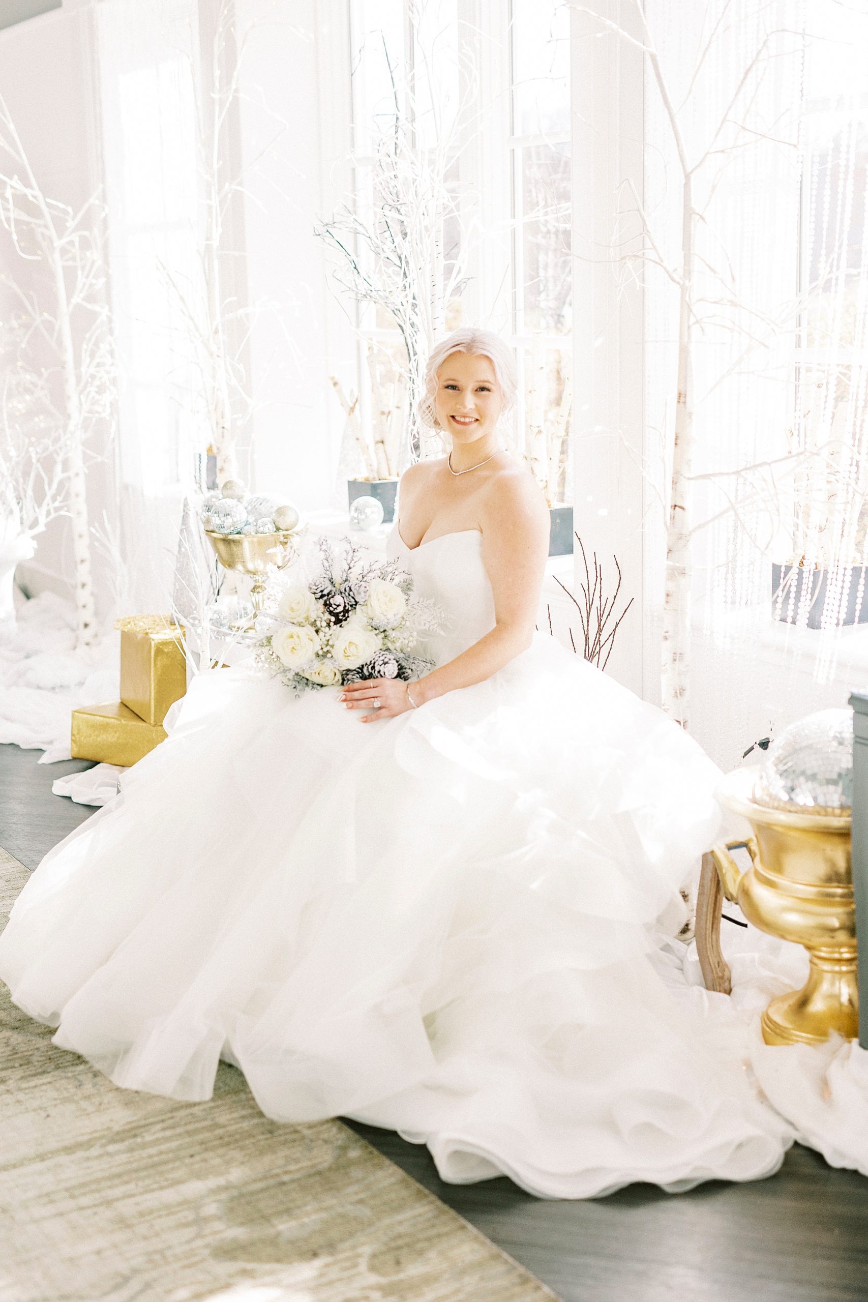 bride sits on seating area with gold seats holding winter inspired bouquet 