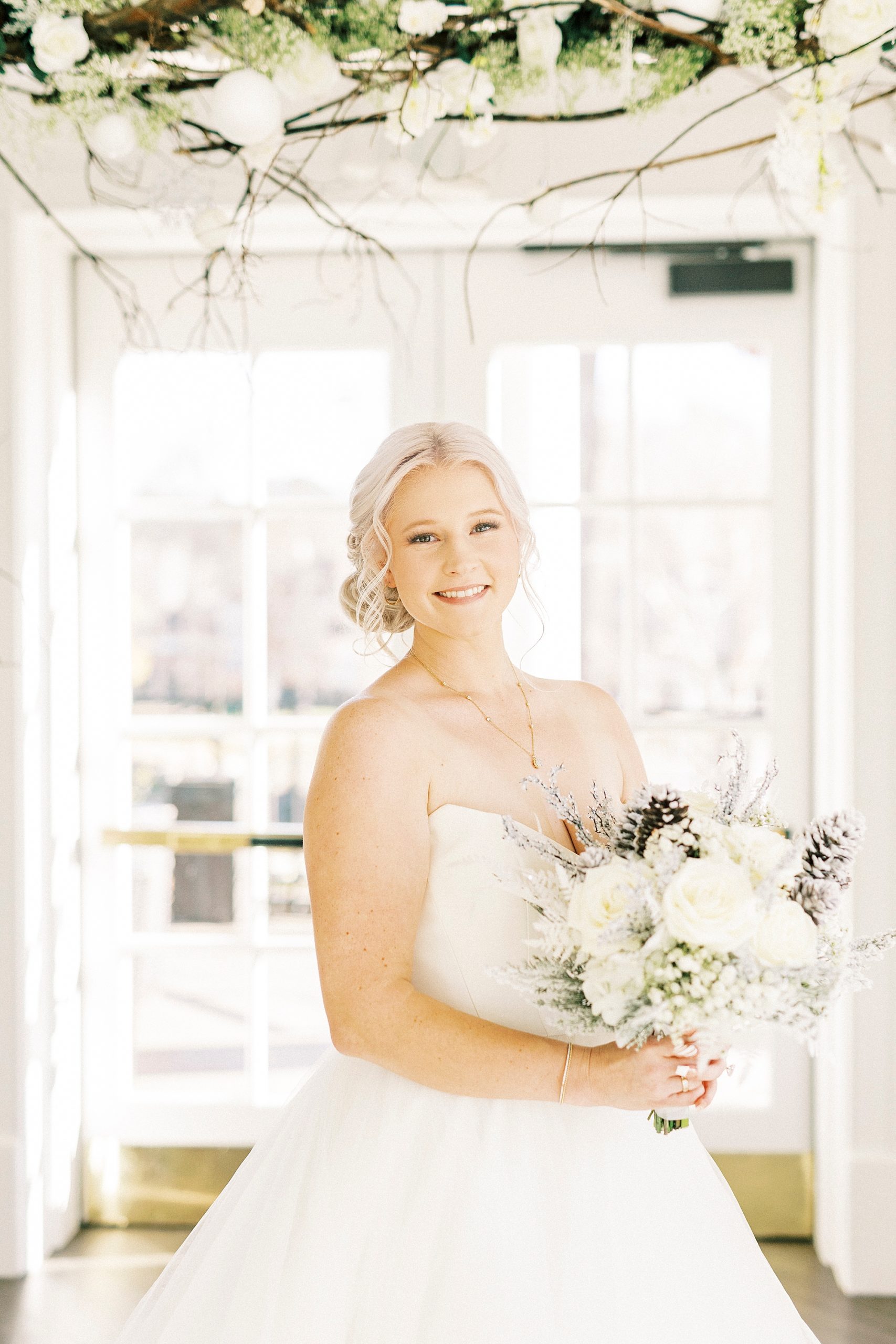 bride poses in strapless gown with winter bouquet inside River Run Country Club