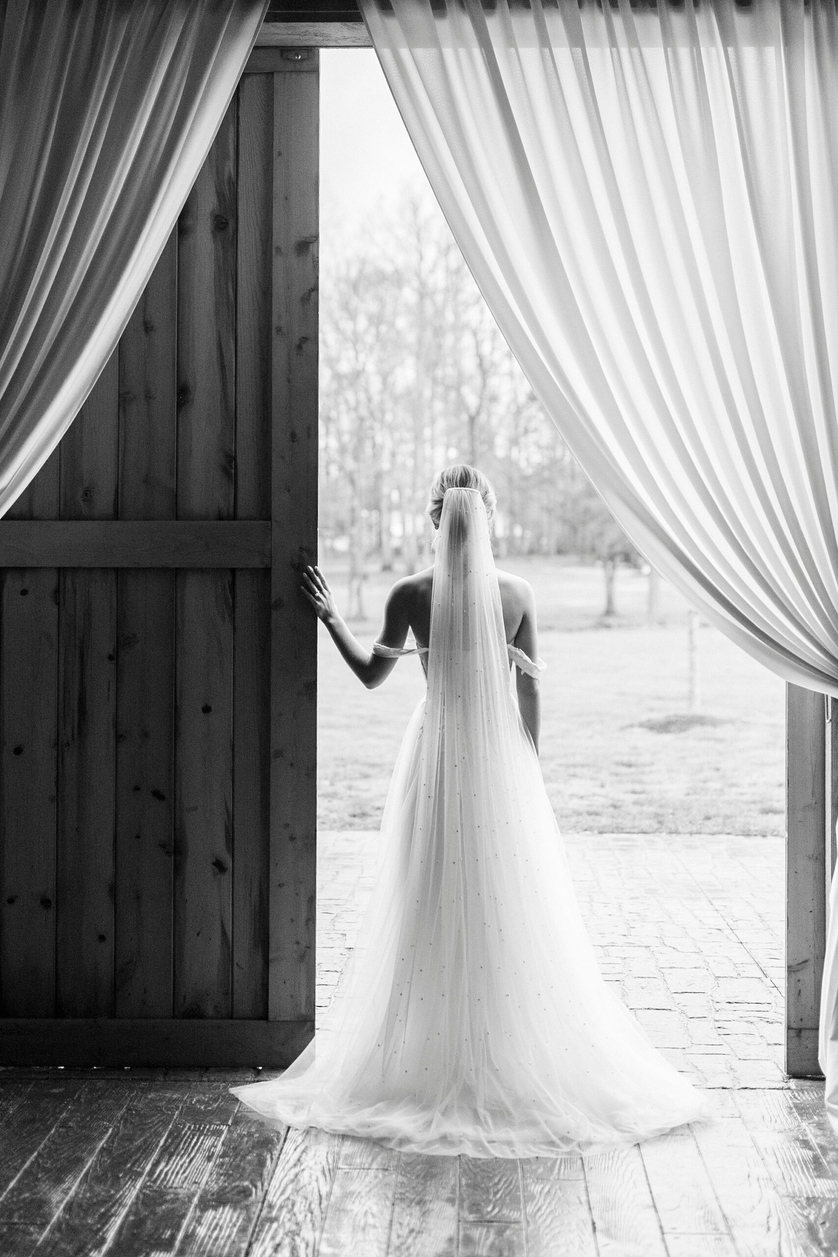 bride stands in doorway of barn looking at field at The Farmstead