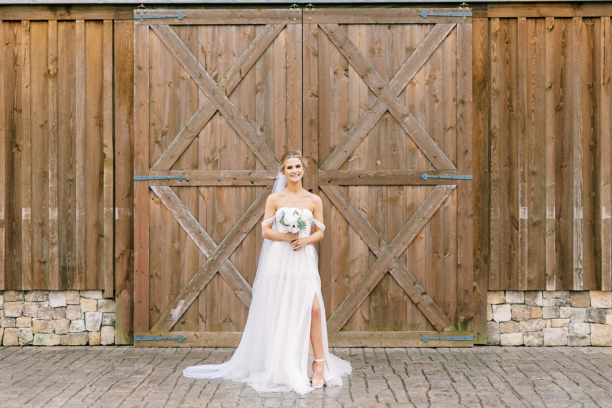 bride poses in wedding dress holding white bouquet by barn doors