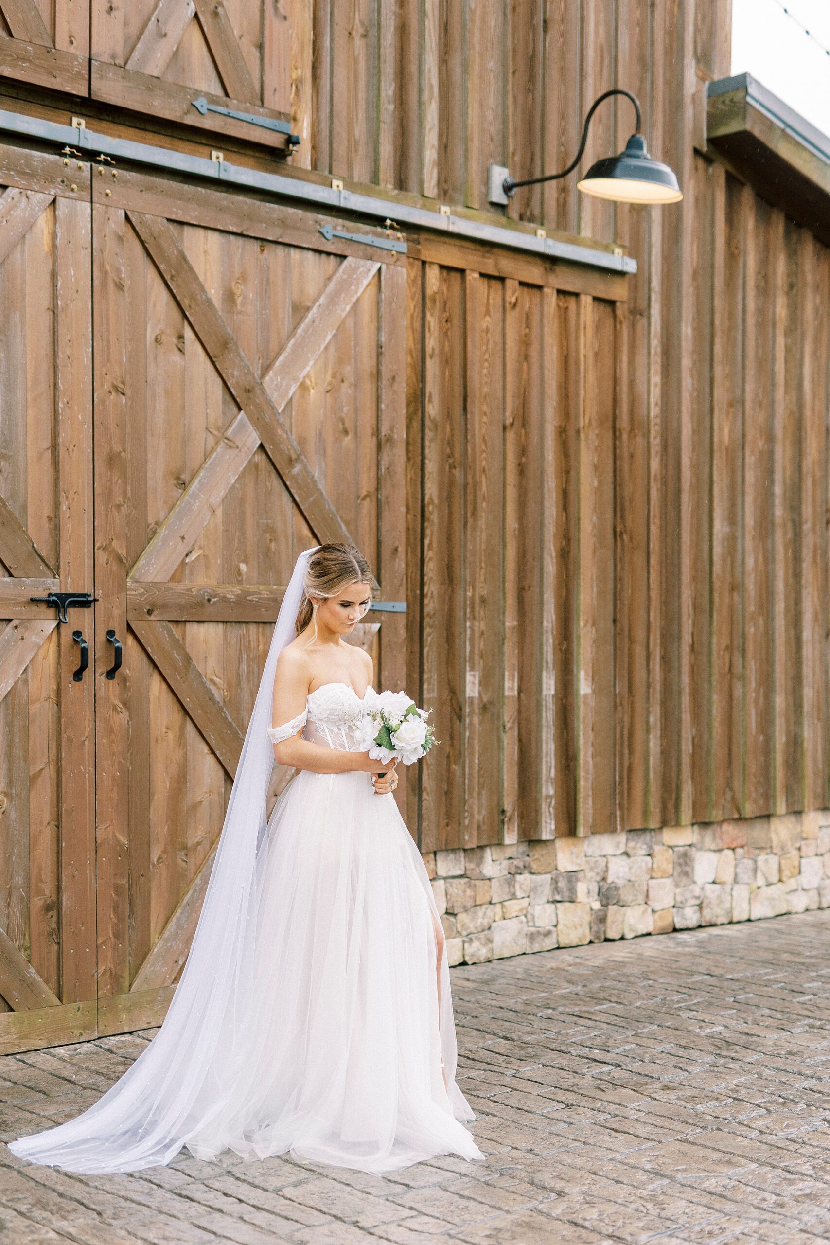bride looks down at bouquet by barn doors at The Farmstead