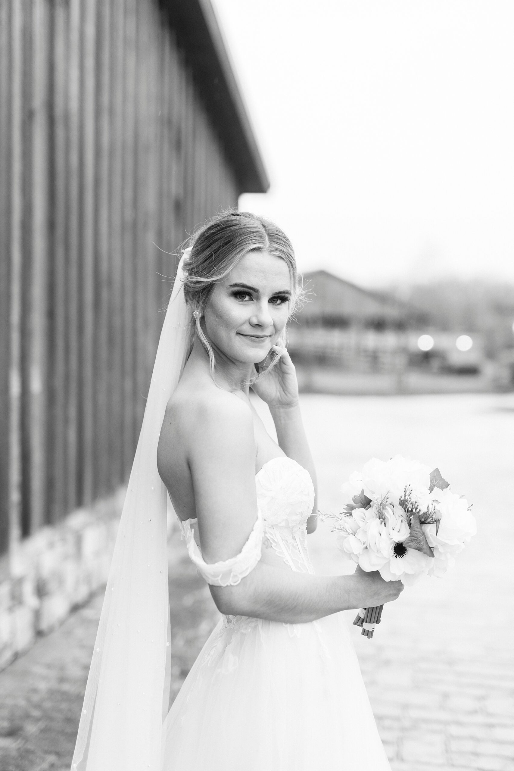 black and white bridal portrait at The Farmstead with bride standing by barn 