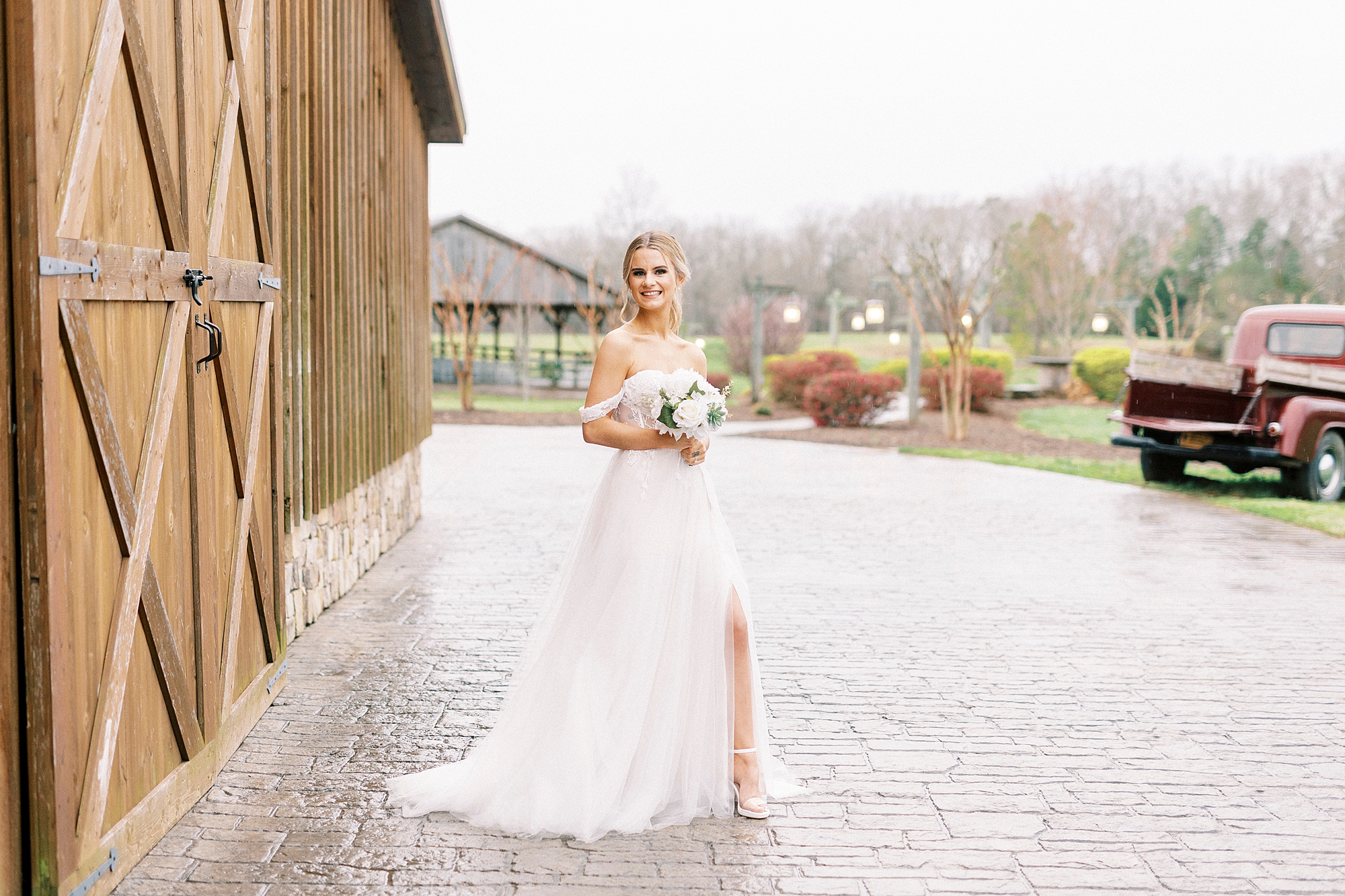 bride poses with leg poking out of dress slit by barn at The Farmstead