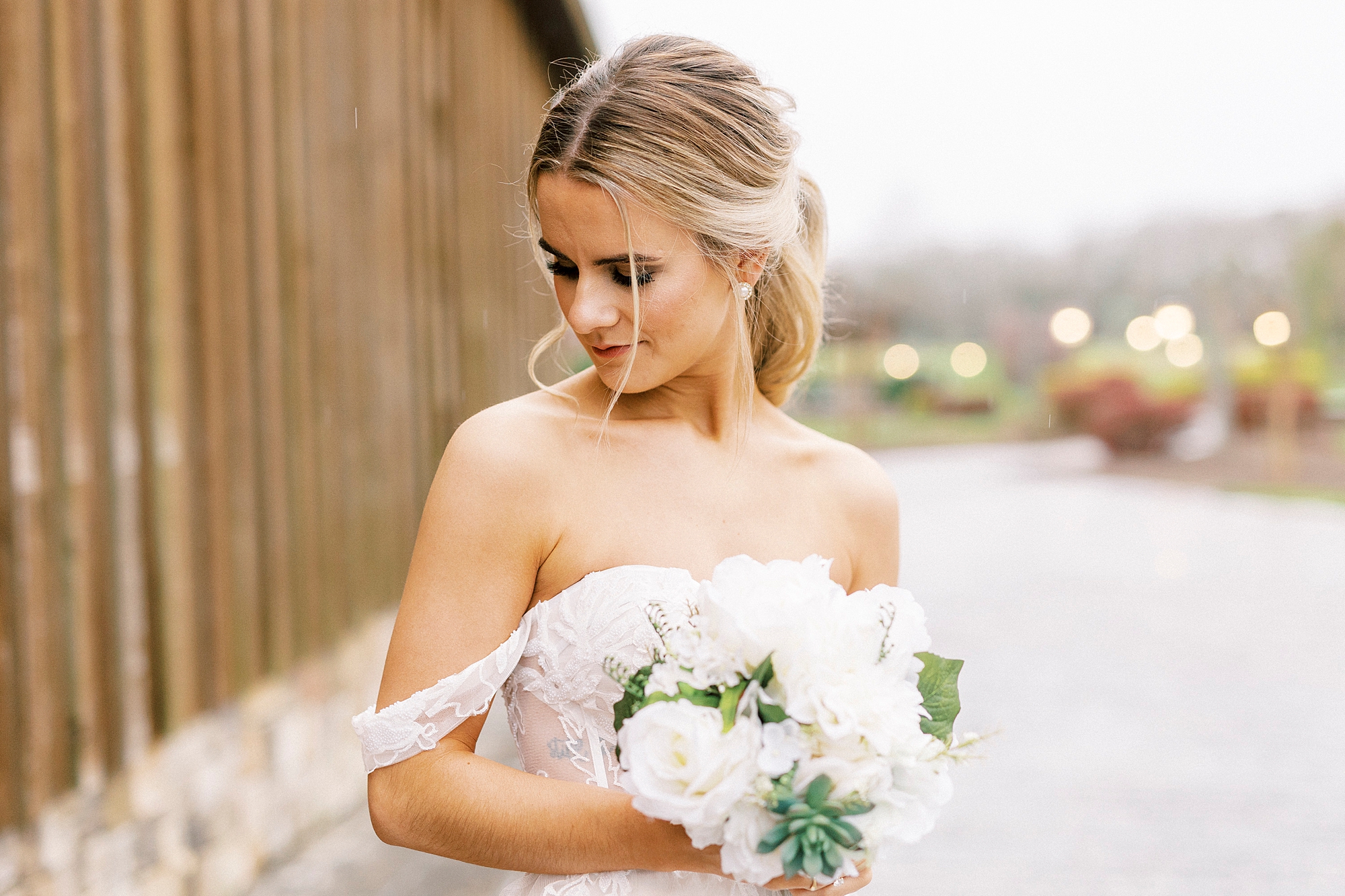 bride in off-the-shoulder wedding gown looks over shoulder holding bouquet of white flowers and succulents 