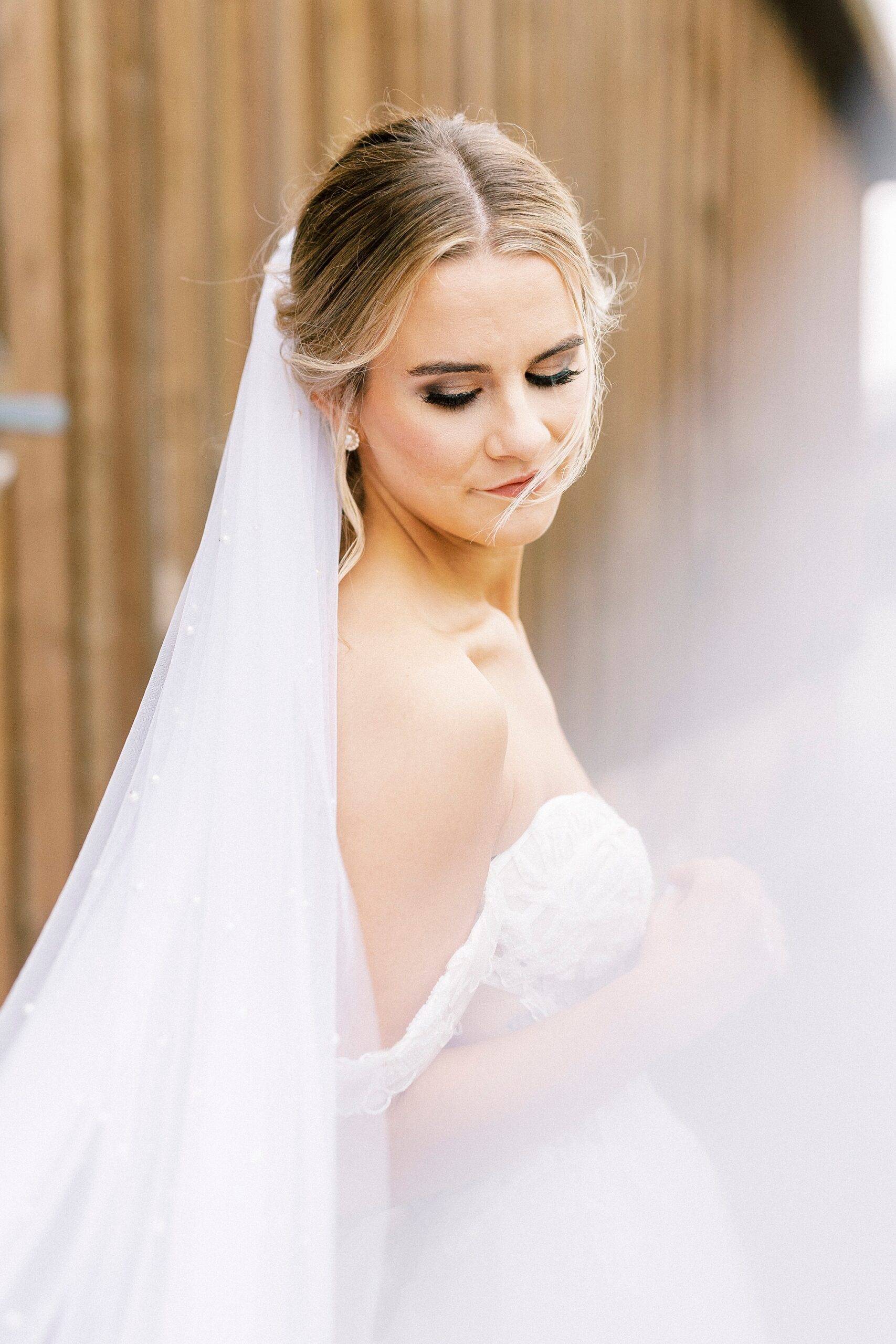 bride looks down with veil pulled up by her during bridal portraits 