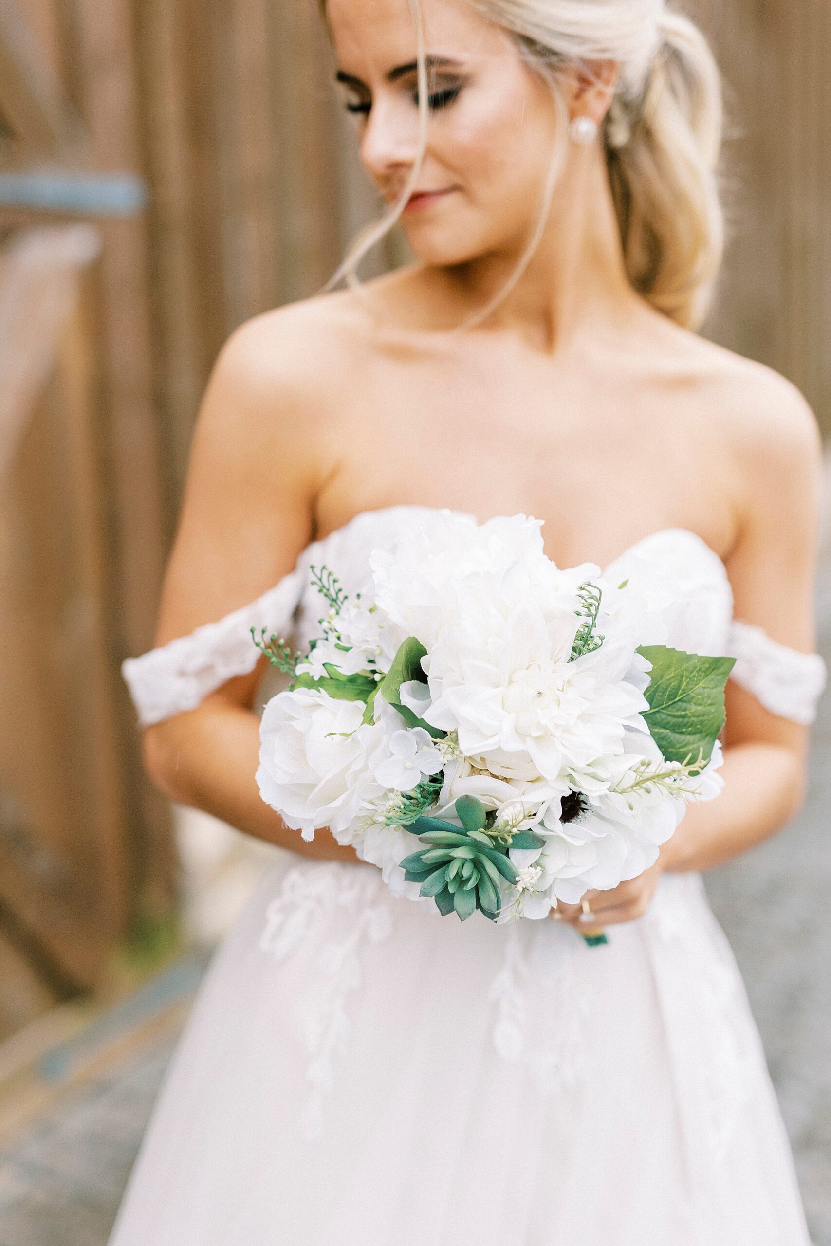 bride holds bouquet of white flowers and succulents by corset top of wedding gown 