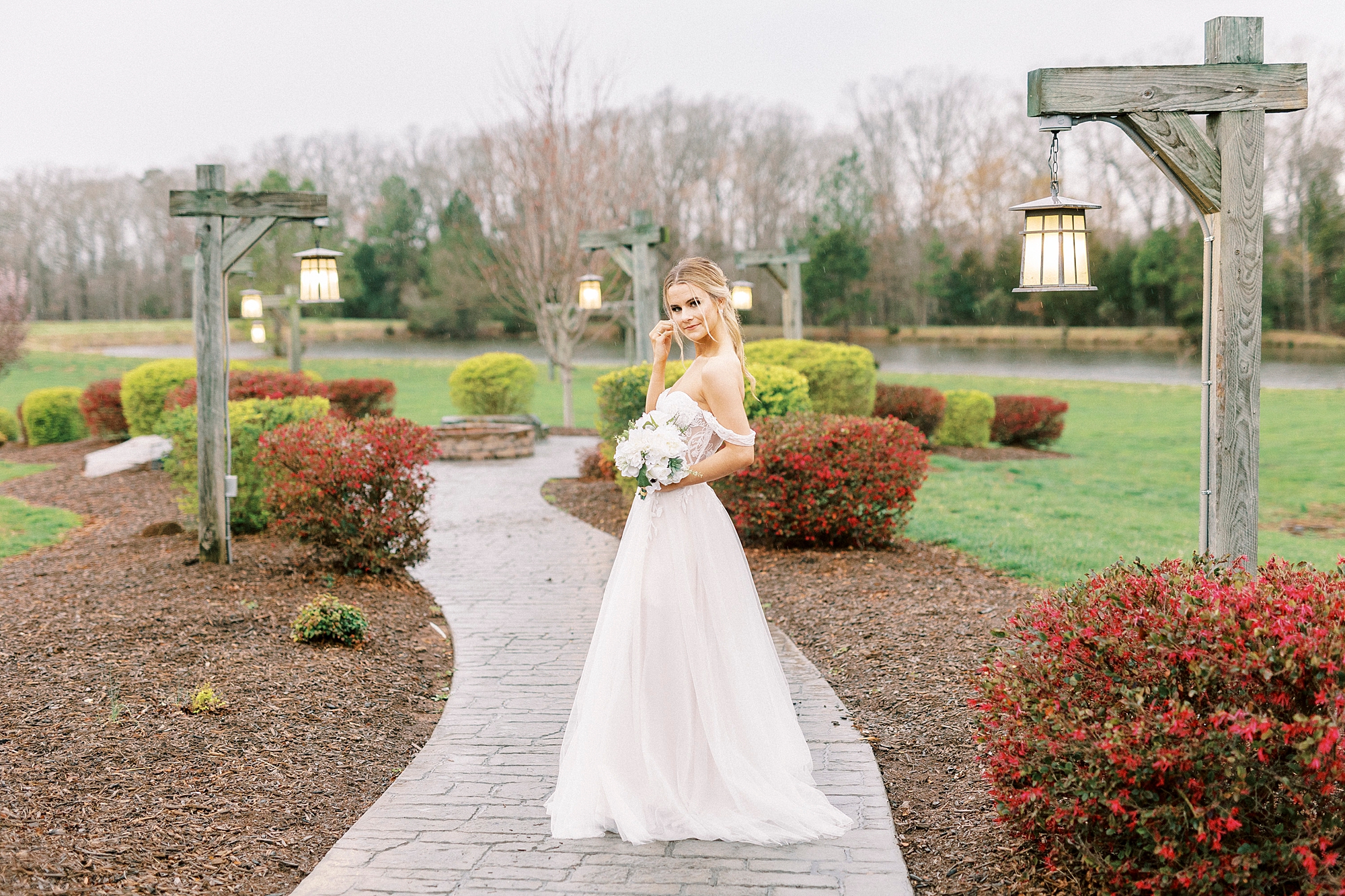 bride poses on walkway at The Farmstead with bouquet in front of her 