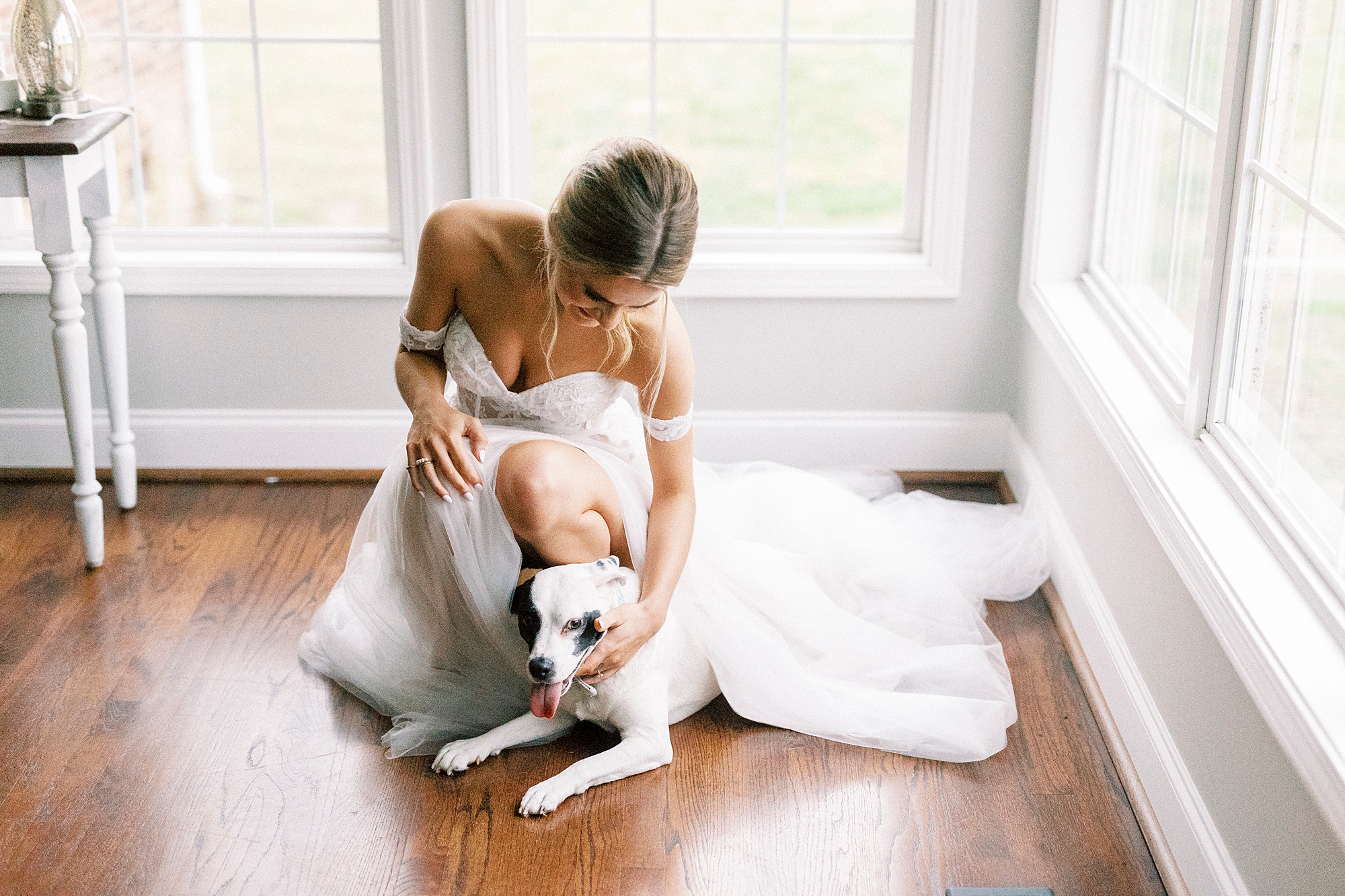bride in wedding gown kneels beside dog, petting him 