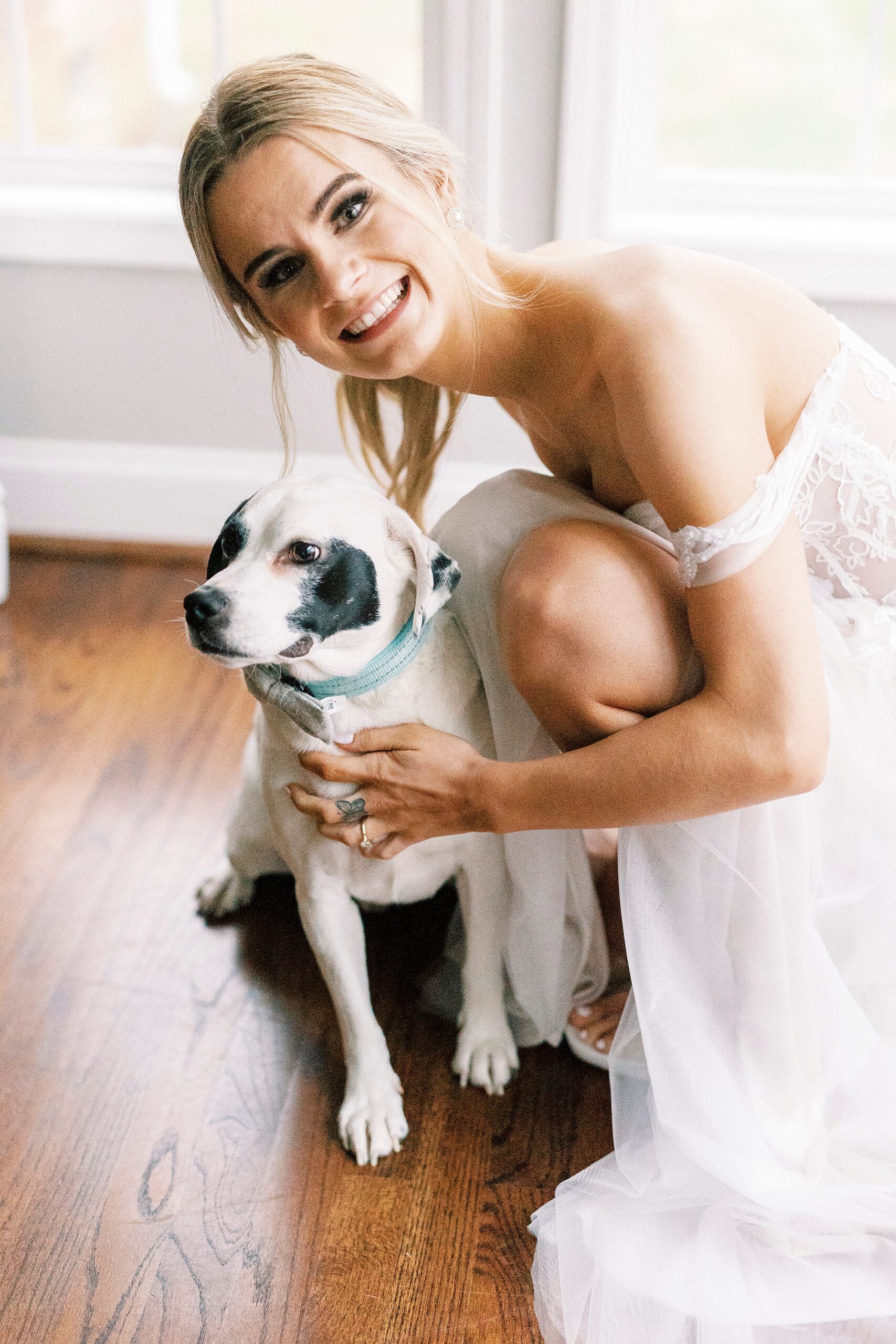 blonde bride in wedding gown kneels by brown and white dog at The Farmstead