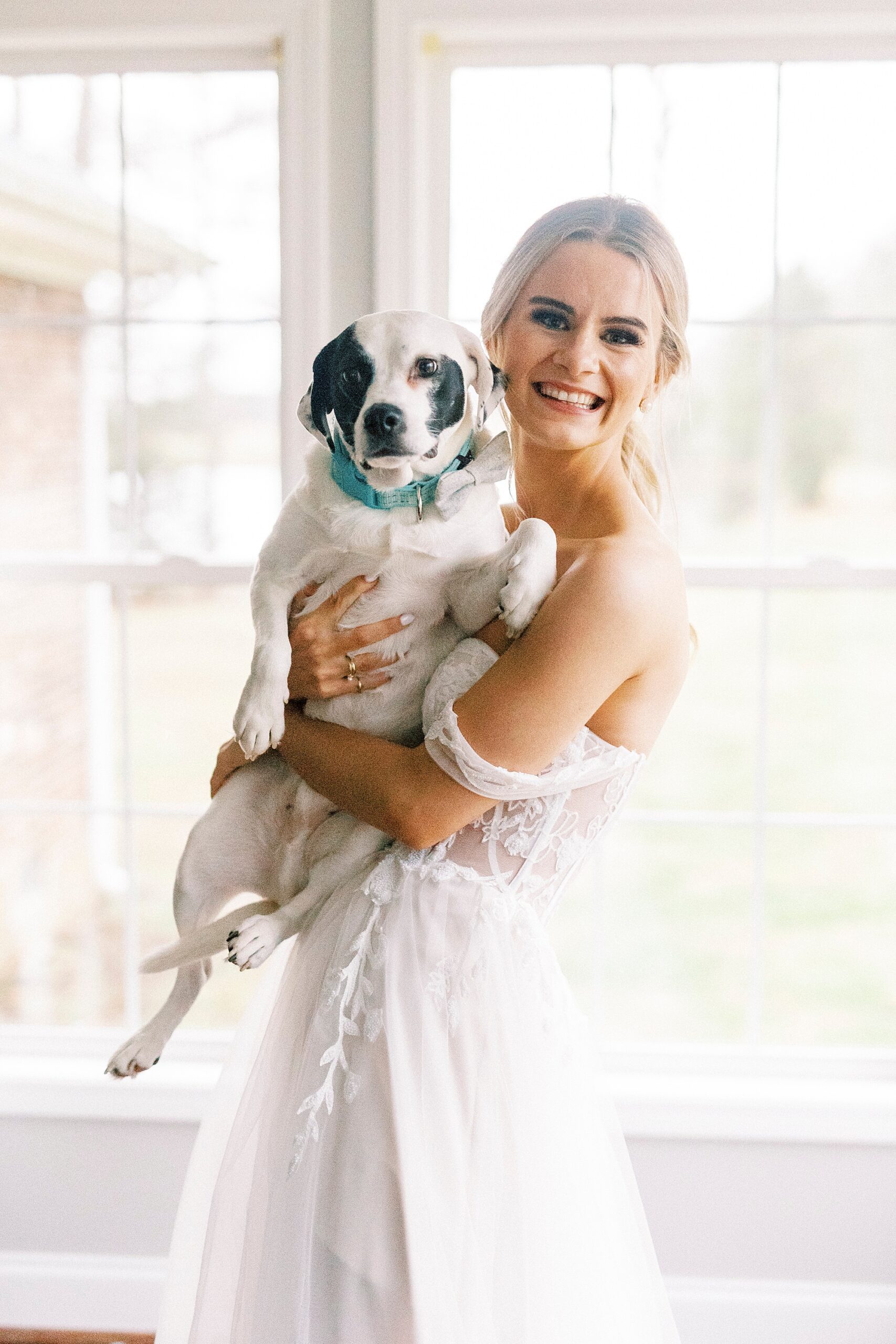 blonde woman in wedding dress holds up brown and white dog 