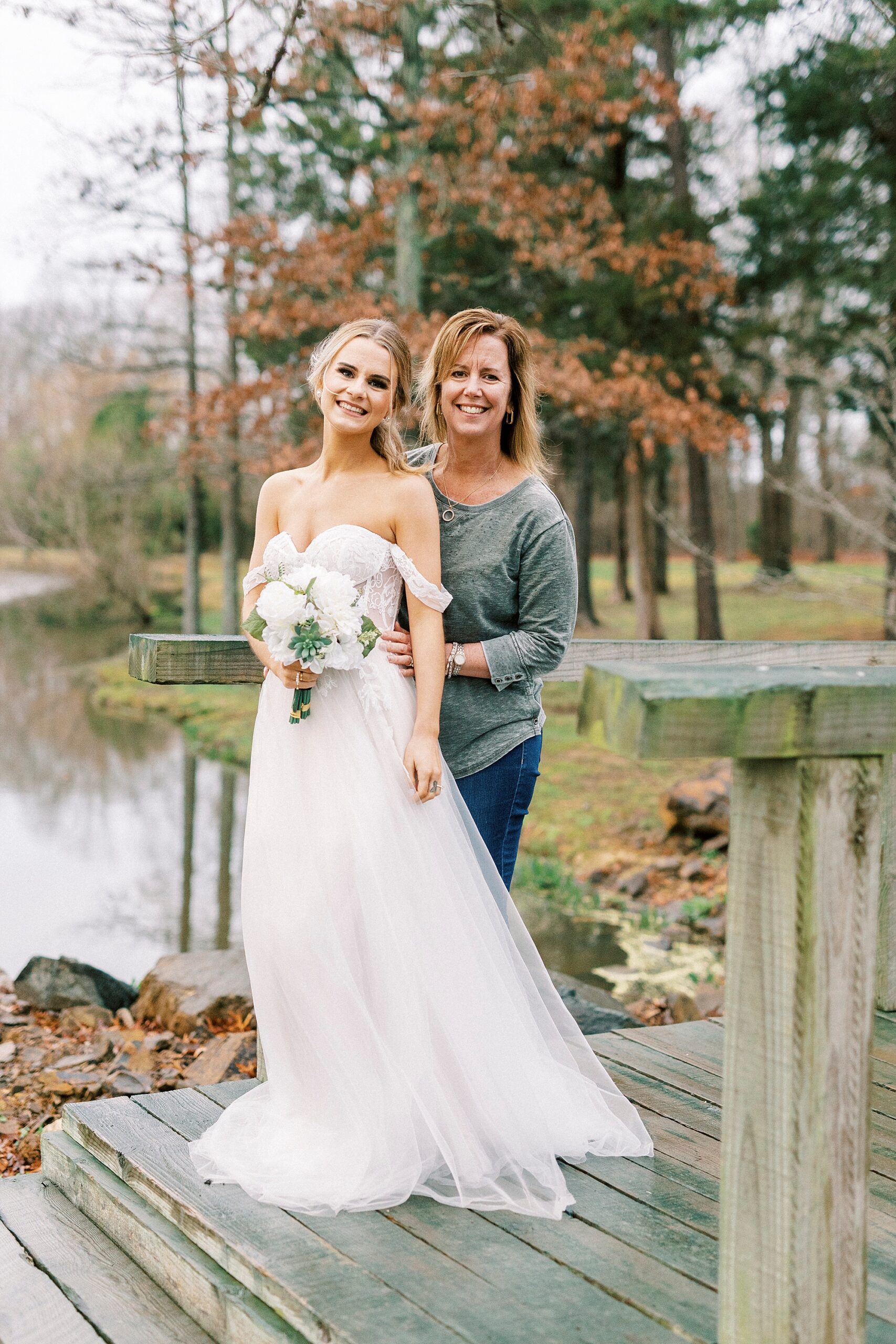 bride poses with mom on wooden dock at The Farmstead