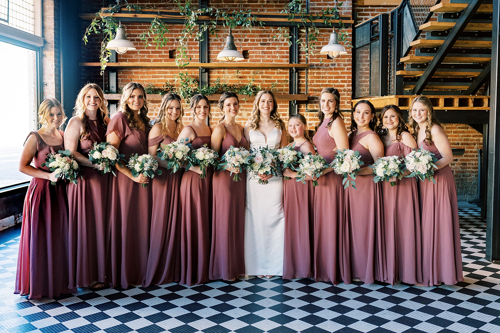 bride poses with bridesmaids in rose gowns on black and white floor