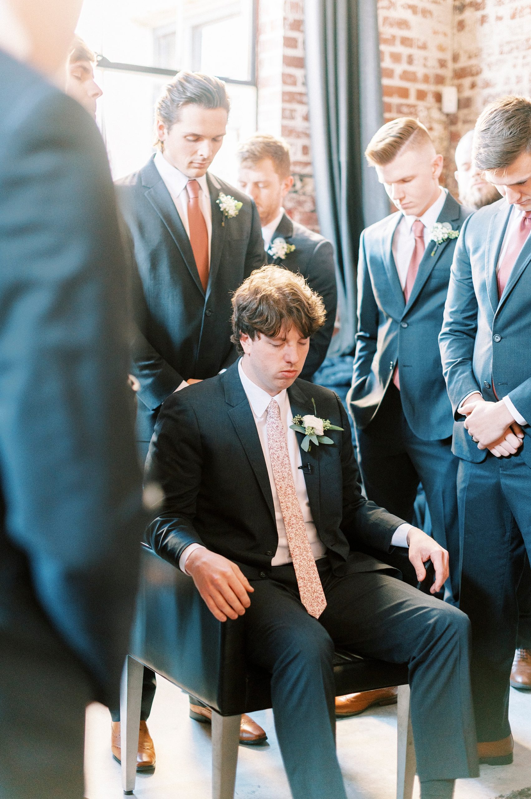 groom closes his eyes praying with his groomsmen 