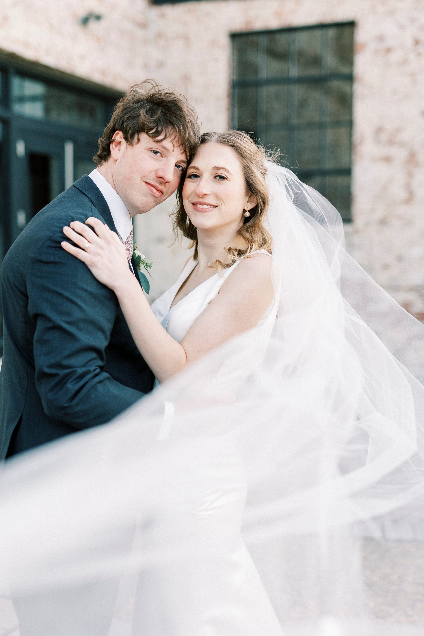 newlyweds lean heads together with veil around them at the Cadillac Service Garage