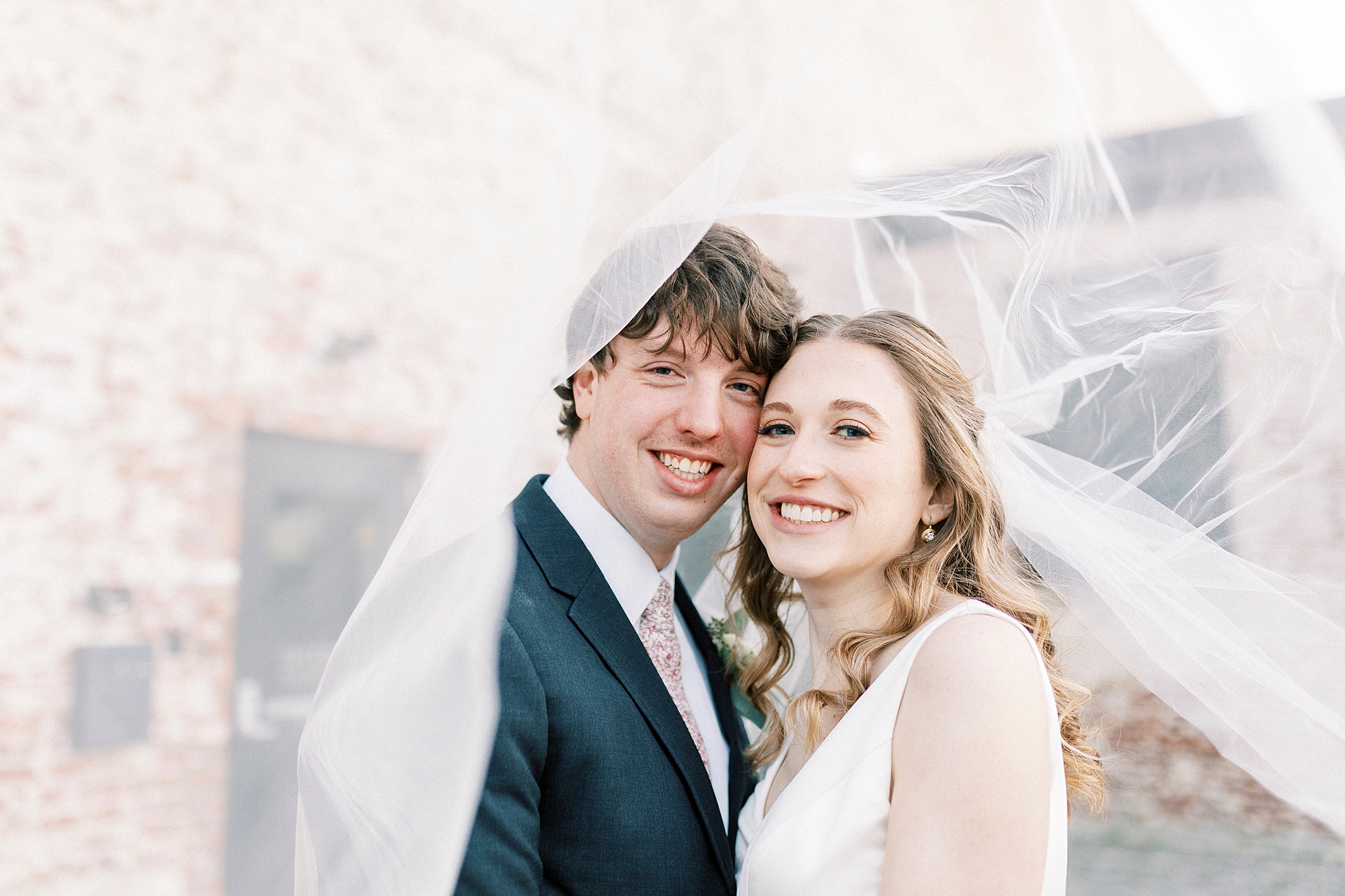 newlyweds lean heads together under bride's veil 