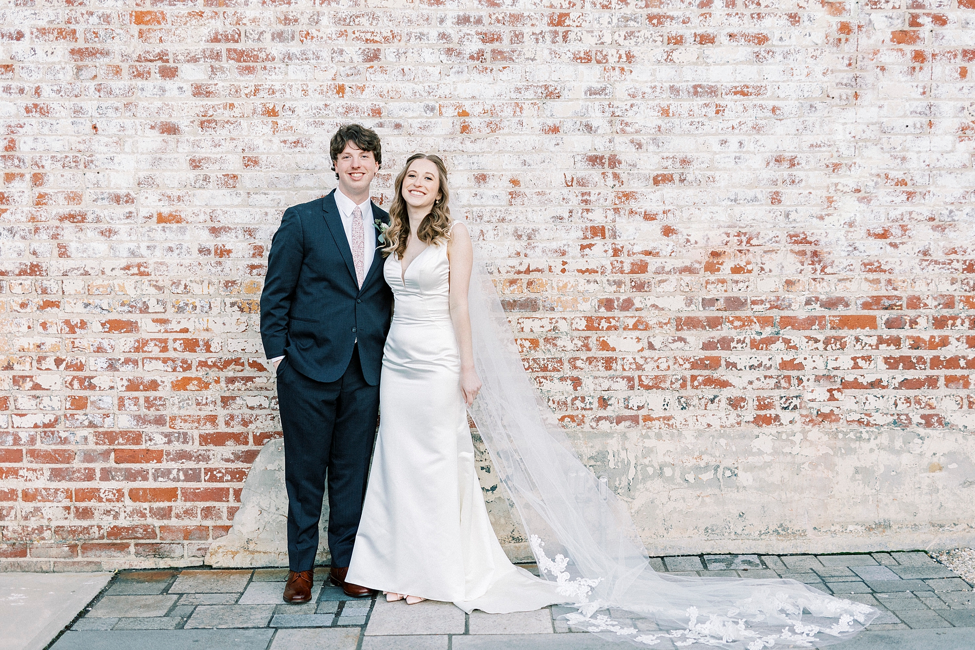 bride and groom stand next to each other hugging in front of brick wall at the Cadillac Service Garage