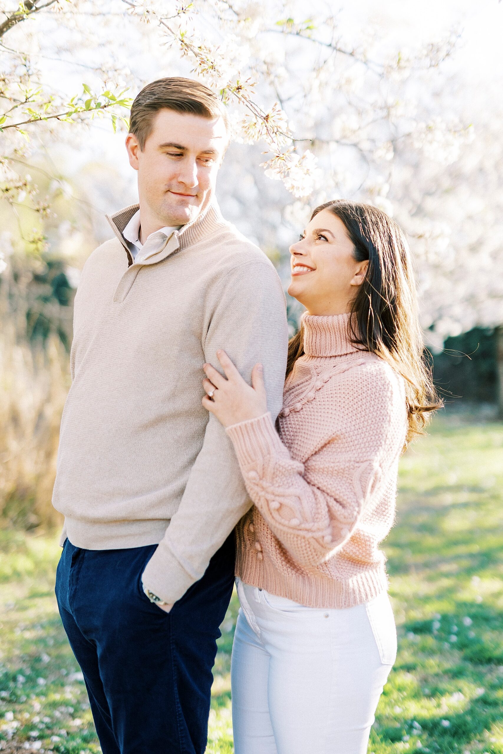woman in pink sweater looks up at man standing by his arm under tree
