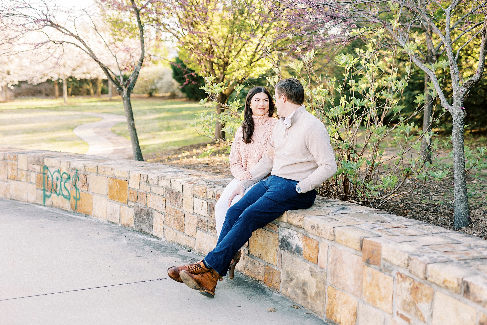 engaged couple sits on stone wall during NC engagement portraits 