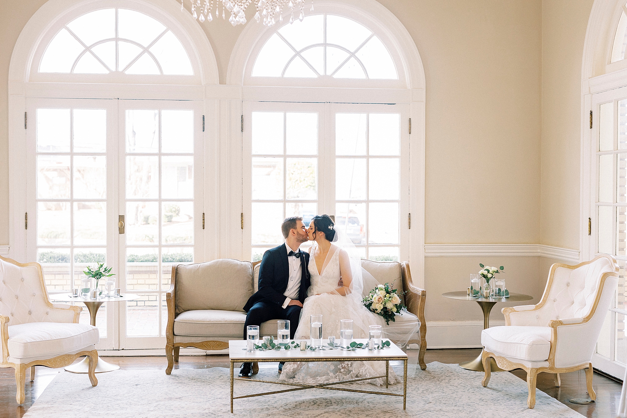 bride and groom kiss on tan couch in front of window in lobby at Separk Mansion