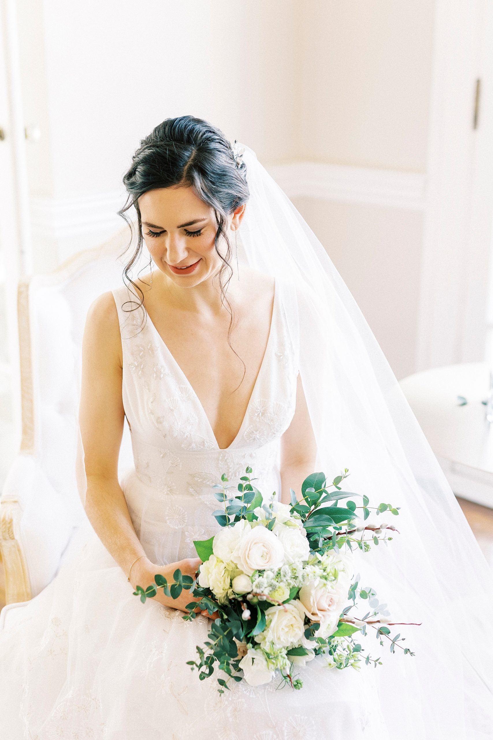 bride sits with white bouquet in lap looking over shoulder 