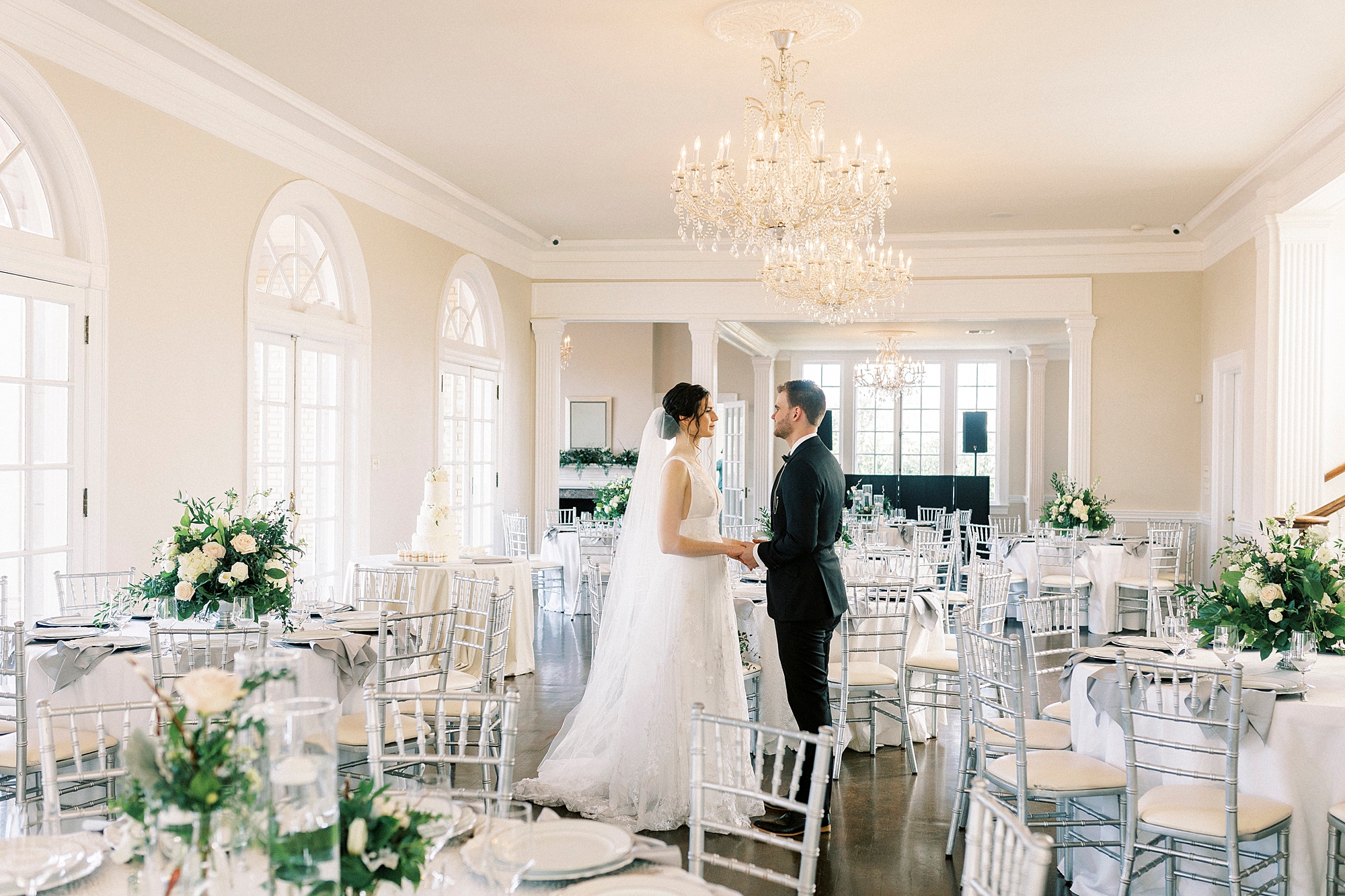 bride and groom holds ands among tables with silver chivari chairs 