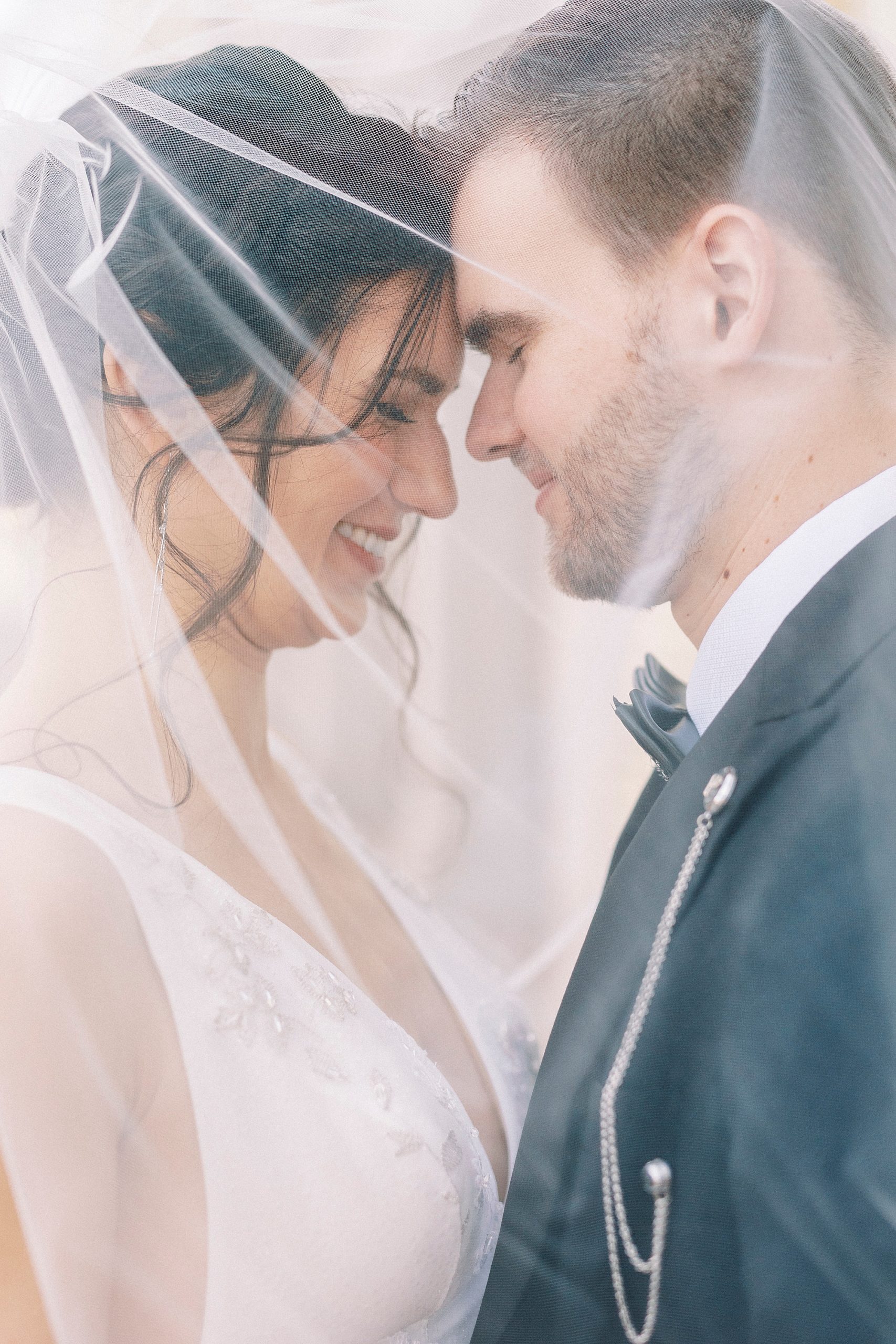 bride and groom lean heads together under veil 