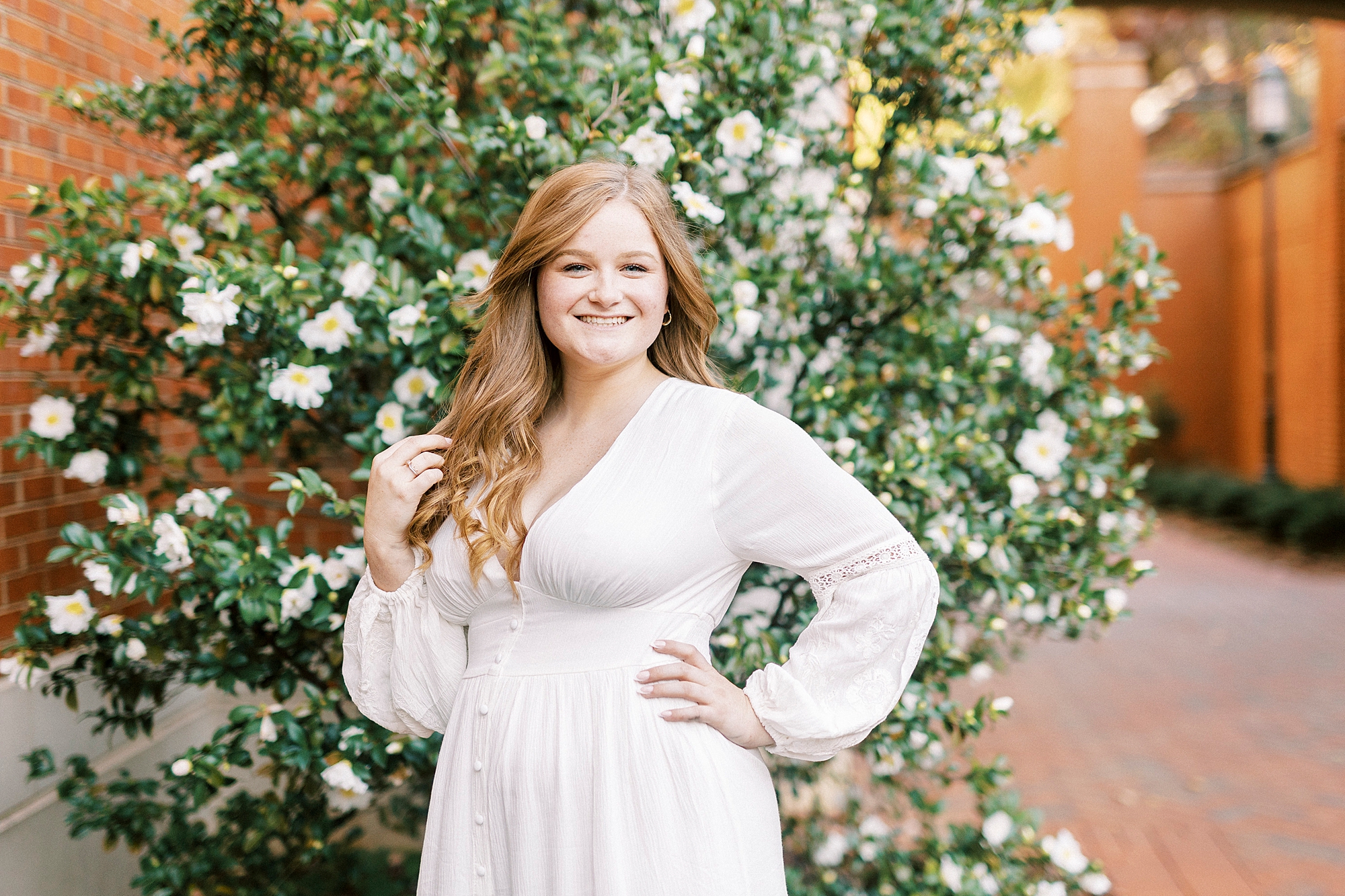 college senior in white dress poses by white flowers at UNC Charlotte