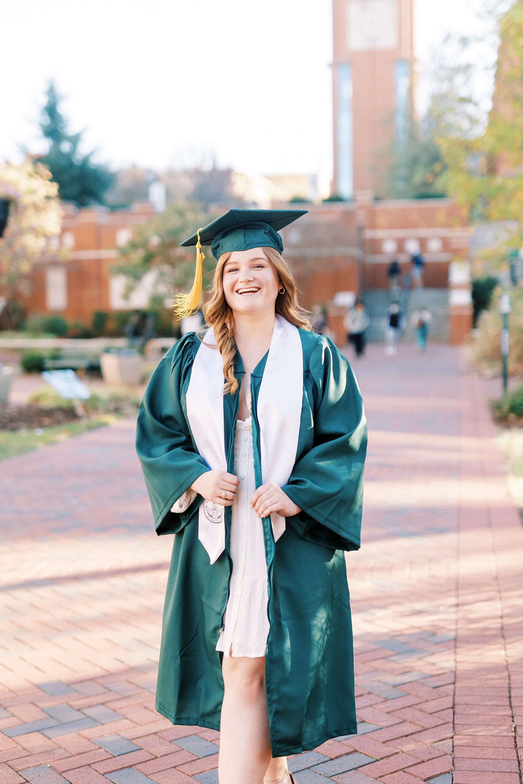 senior poses in green cap and gown during UNC Charlotte senior portraits 