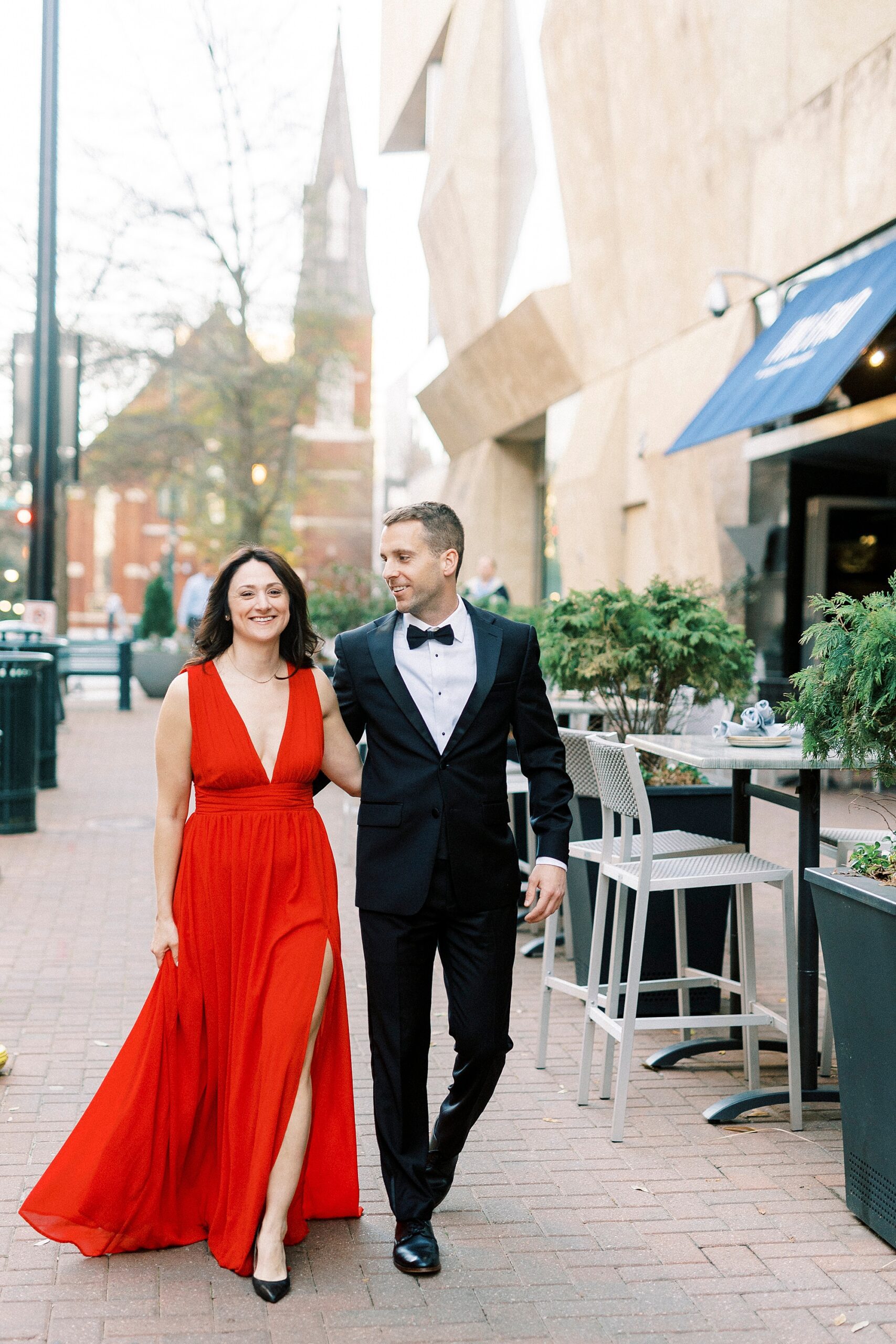 engaged couple holds hands walking down street in classy attire 