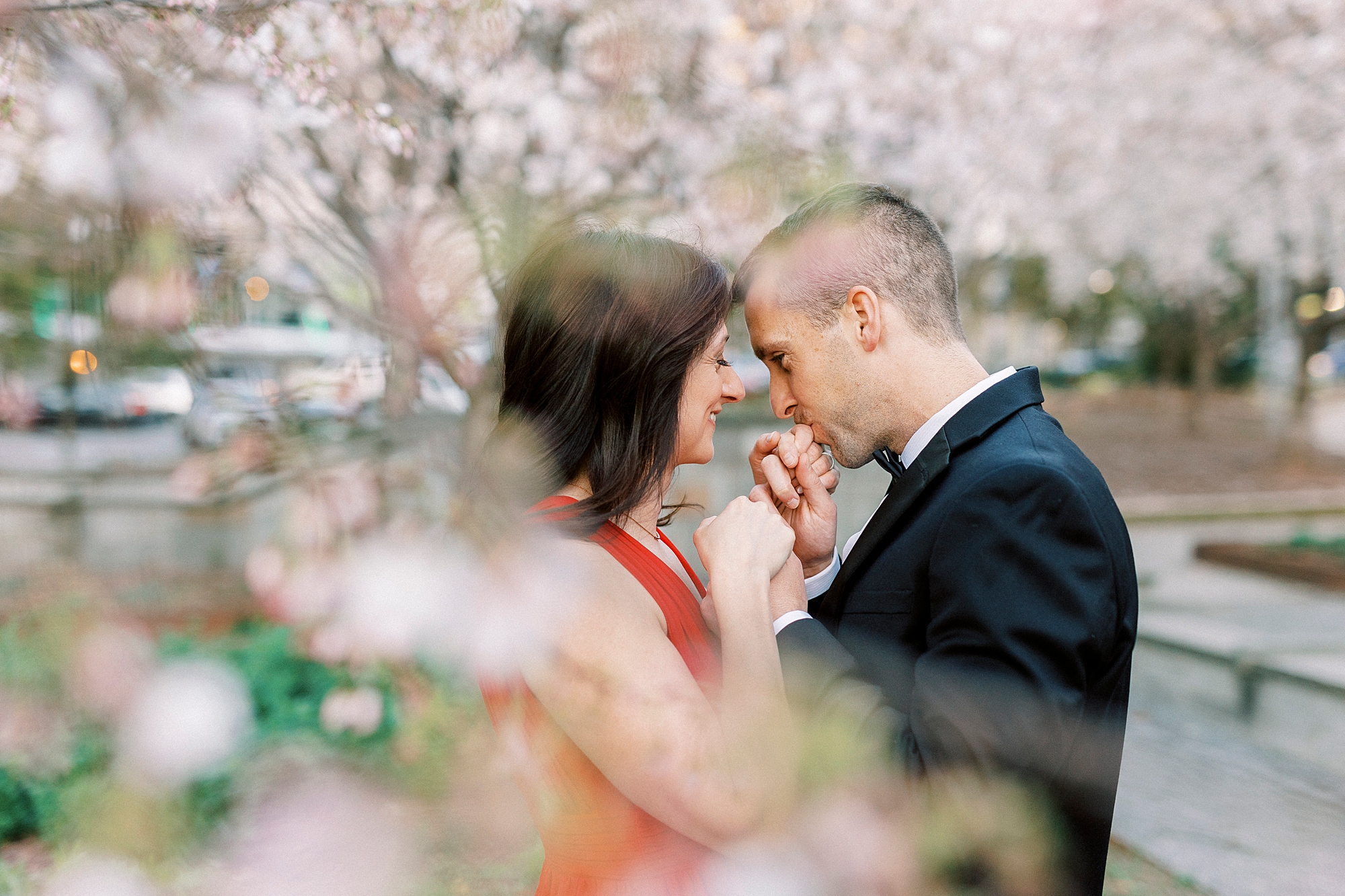 man kisses woman's hand under tree during spring engagement session in Romare Bearden Park
