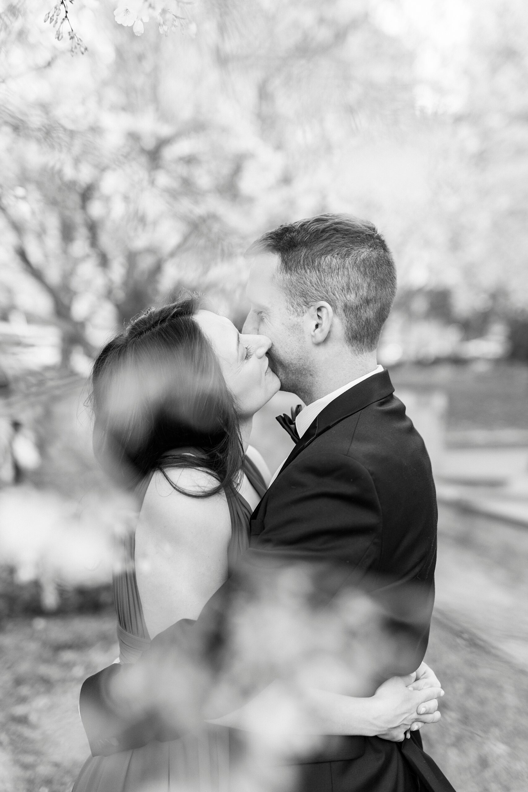 black and white portrait of couple kissing between trees at Romare Bearden Park