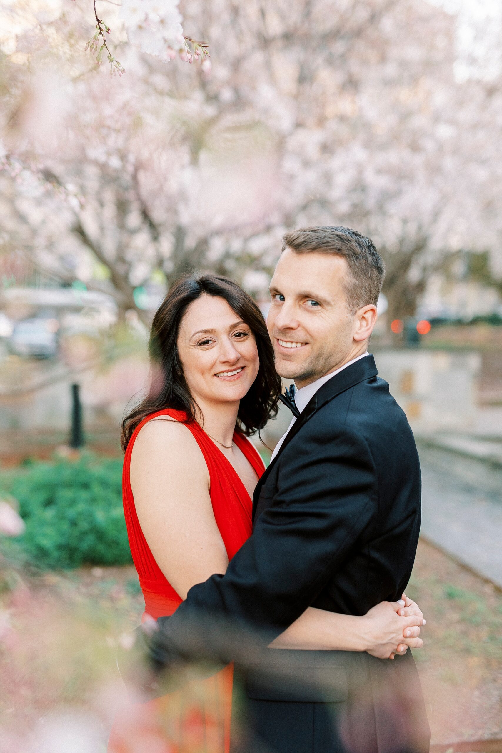 engaged couple hugs between branches of cherry blossom tree
