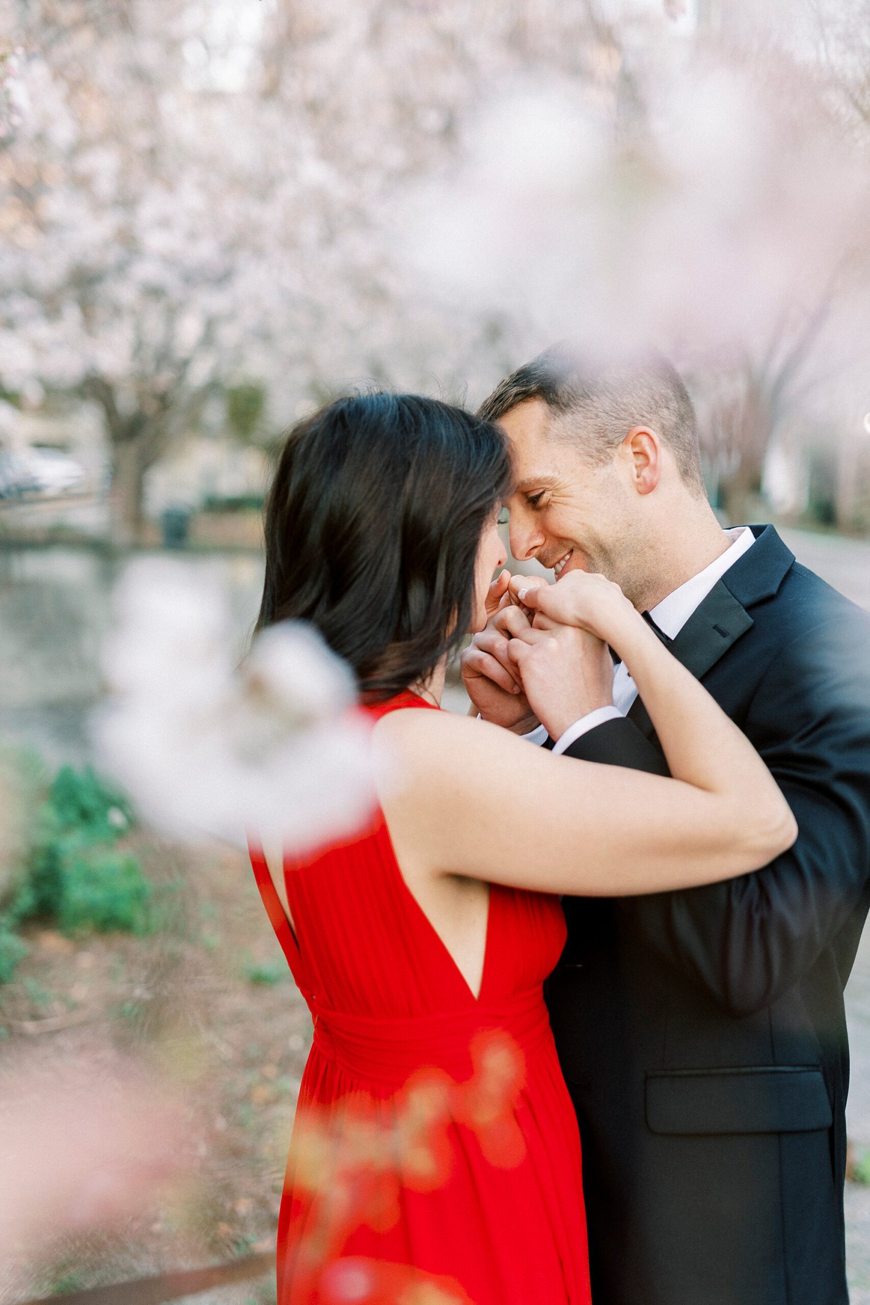 man kisses hand of woman in red dress during spring engagement session 