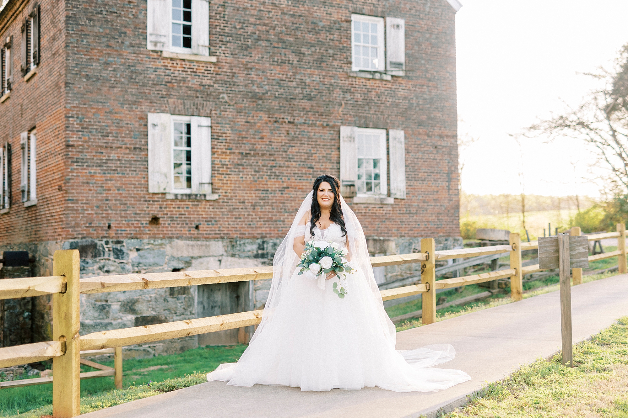 bride holds bouquet of white flowers by brick building during Sloan Park bridal portraits