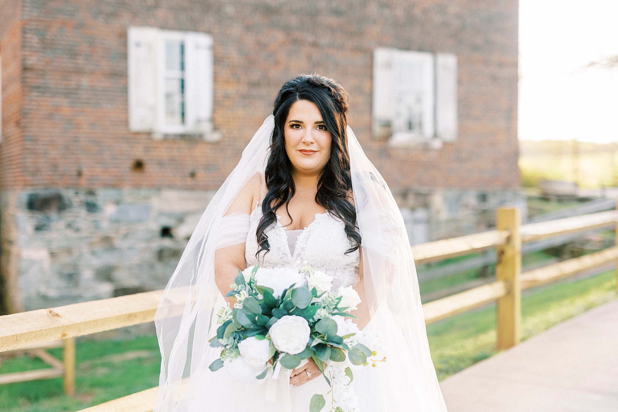 bride holds bouquet of white flowers smiling at camera with veil around shoulders 