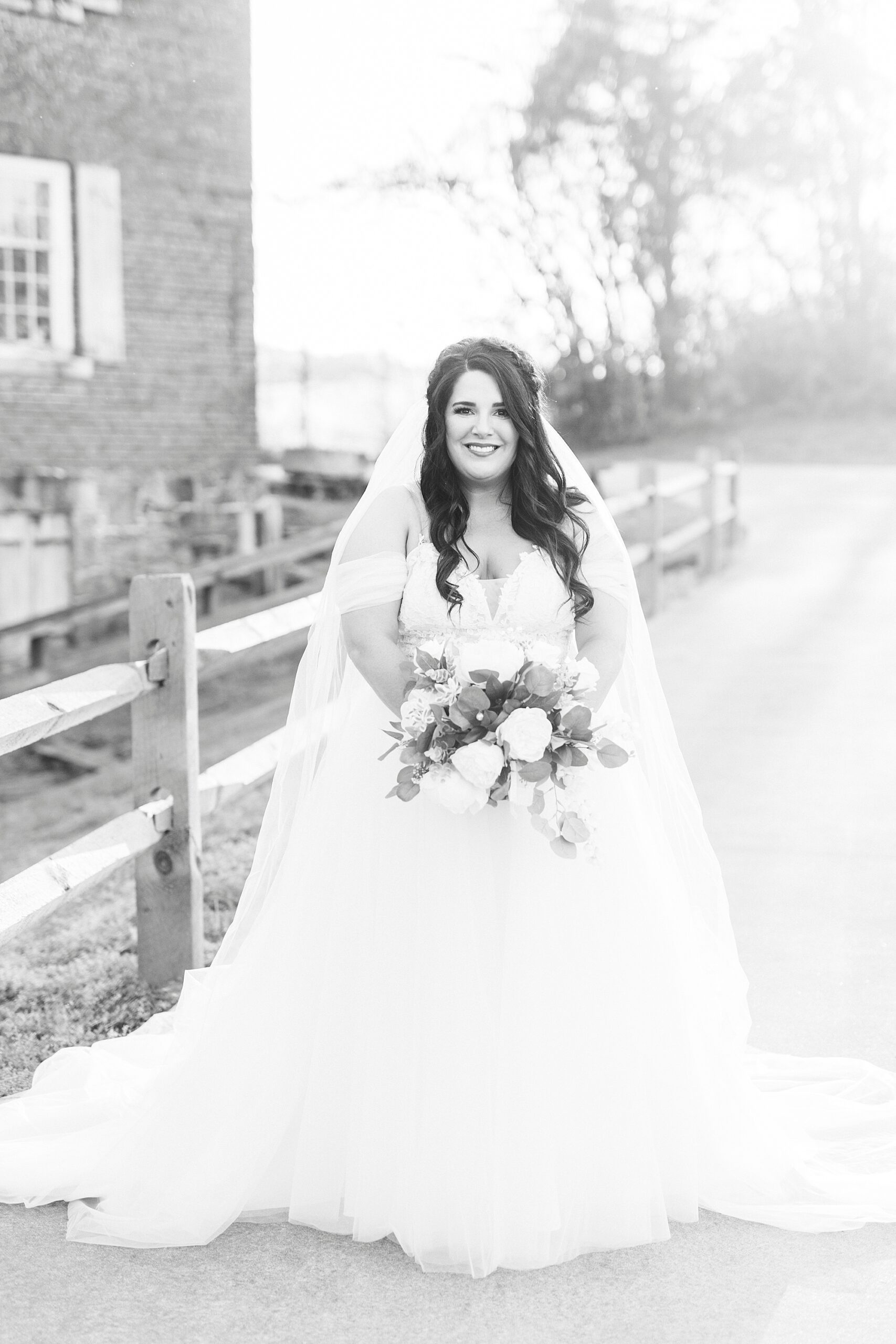 bride stands holding all-white bouquet in black and white photo